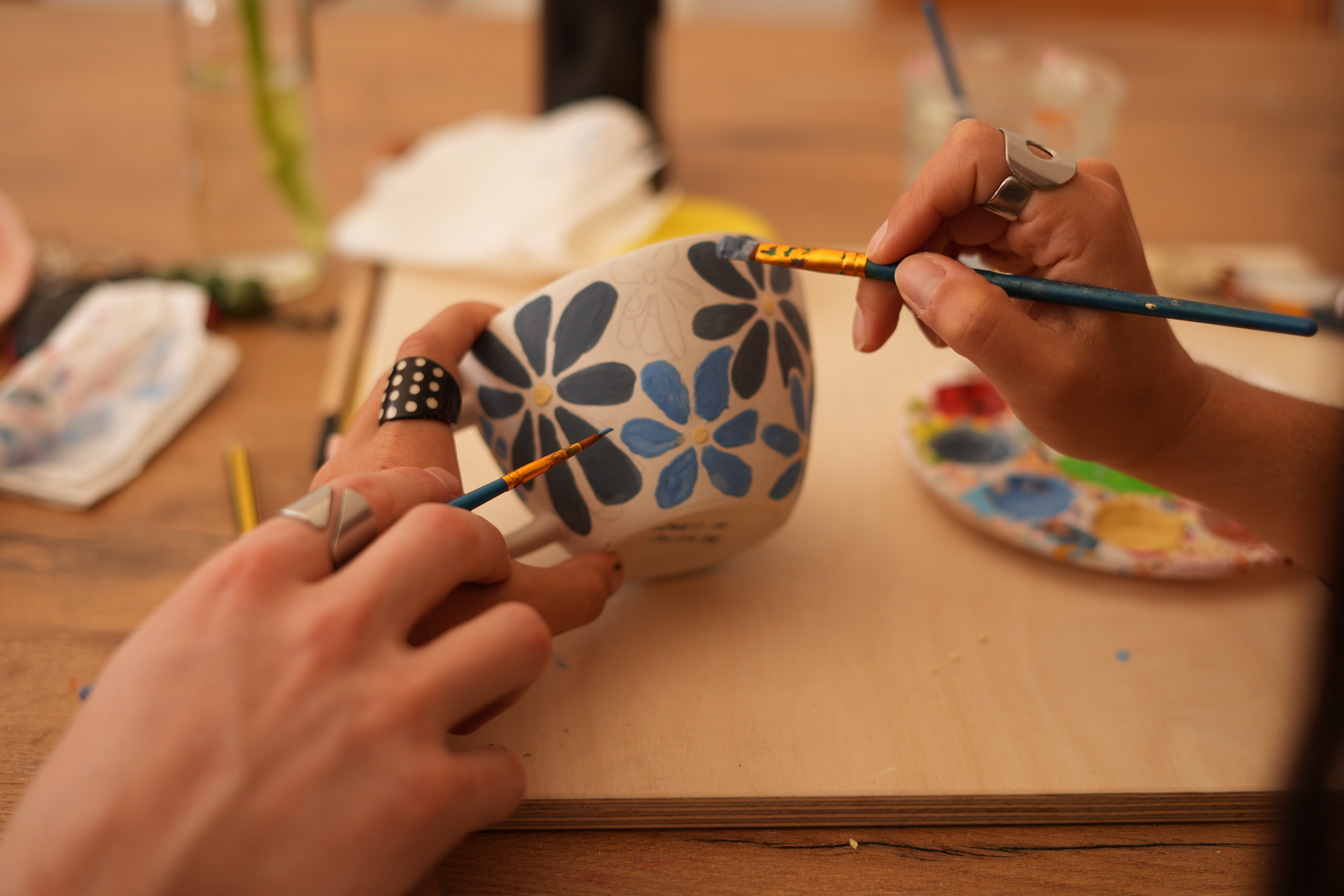 Hands painting floral designs on ceramic cup.