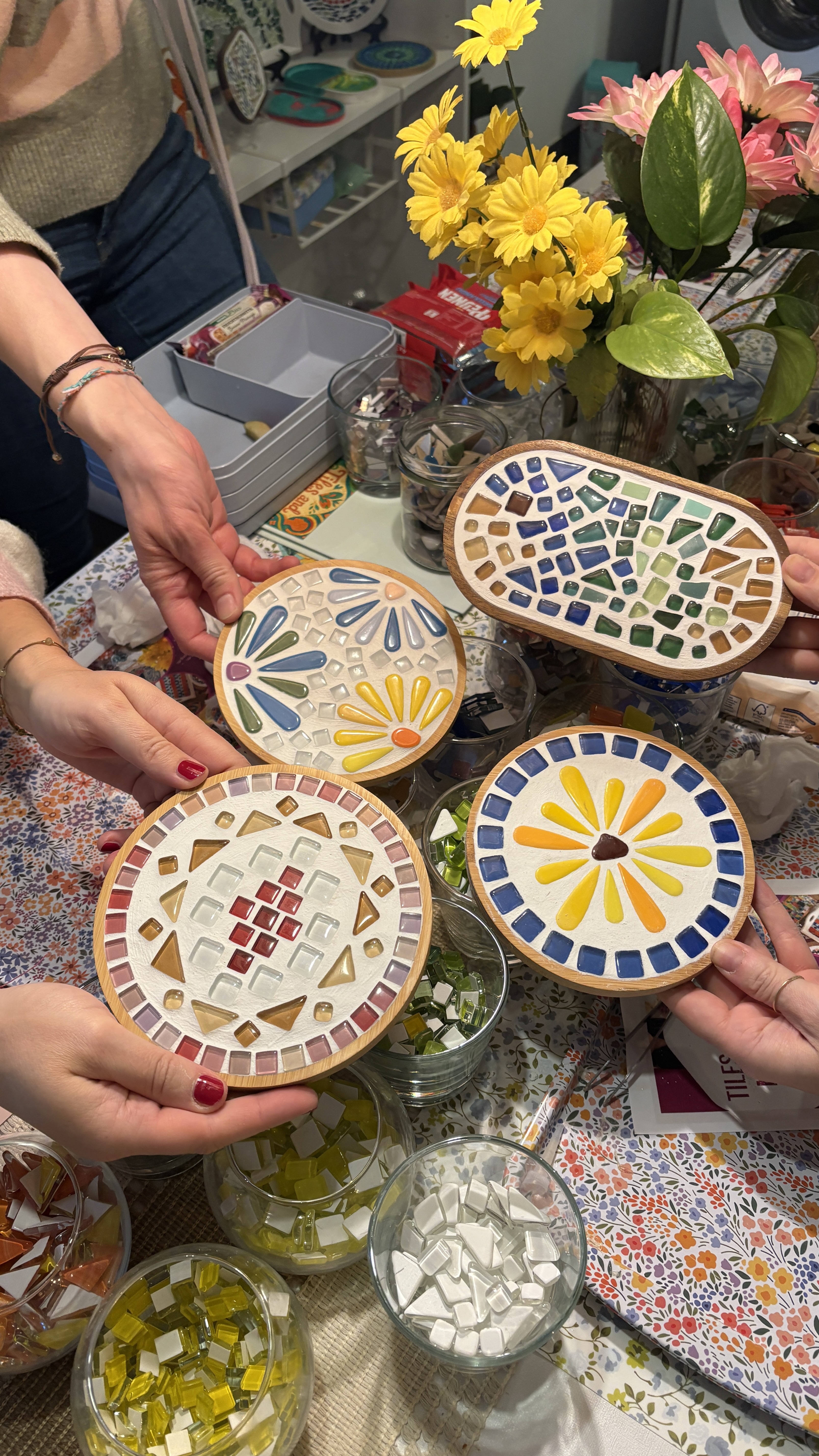 Hände halten bunte Mosaik-Untersetzer auf Tisch.