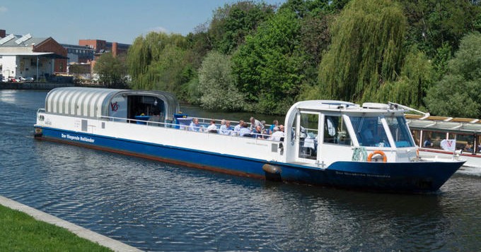 Sightseeing boat cruising along a lush riverside.