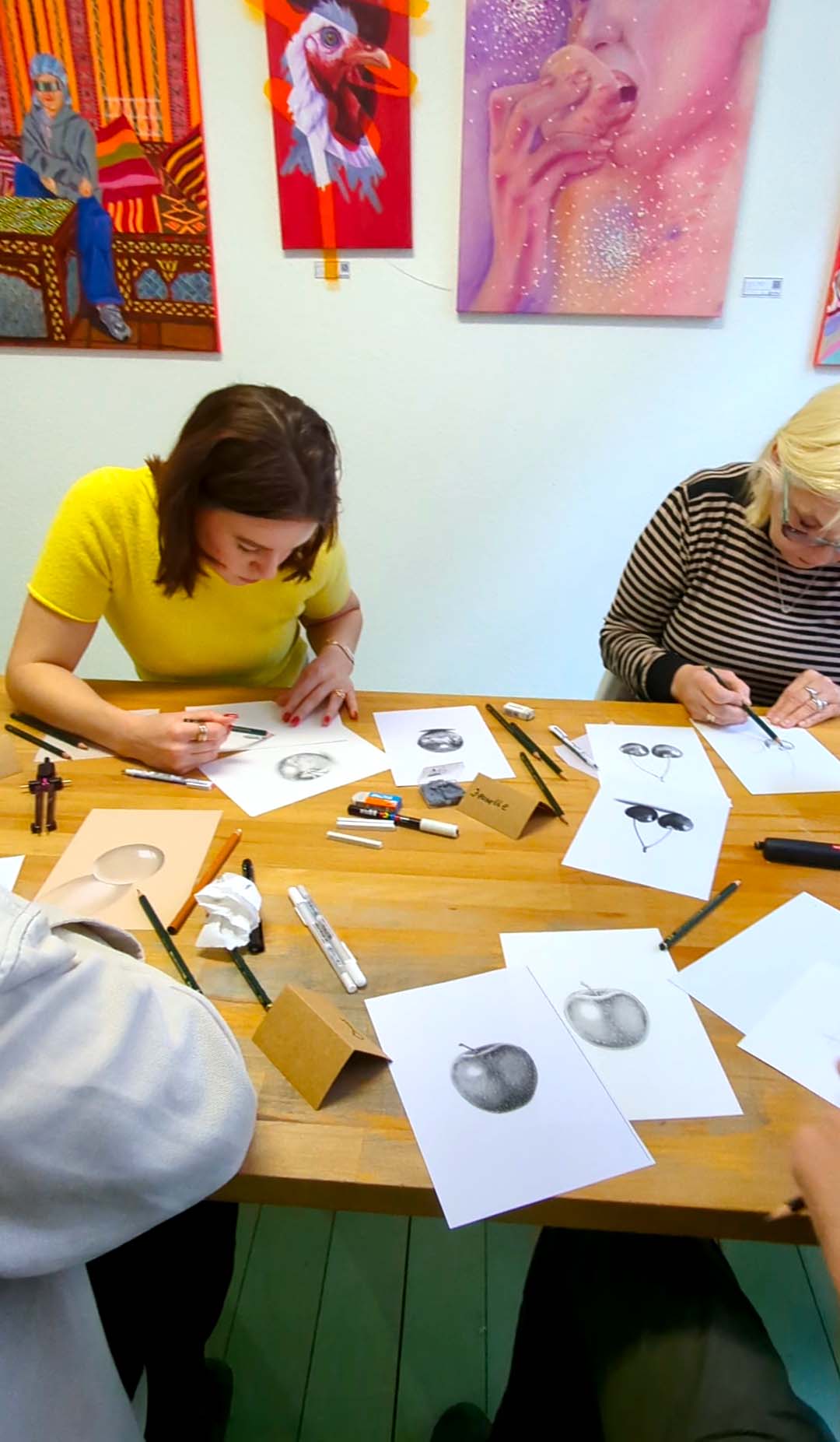 Two women drawing at a wooden table.