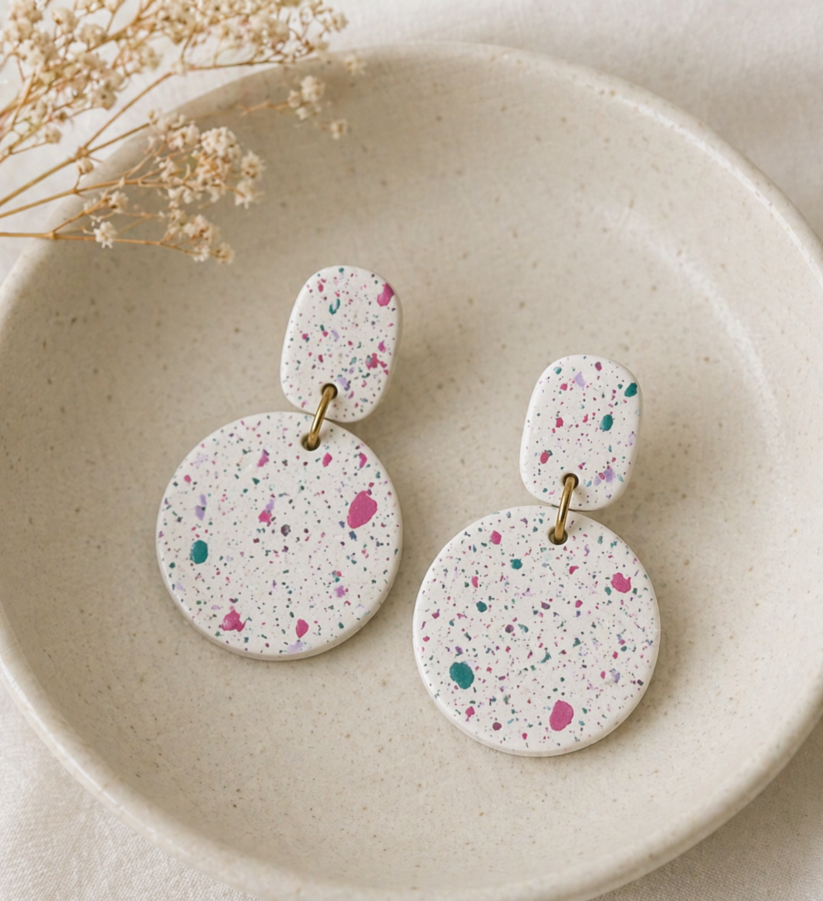 Speckled white earrings in a ceramic dish.