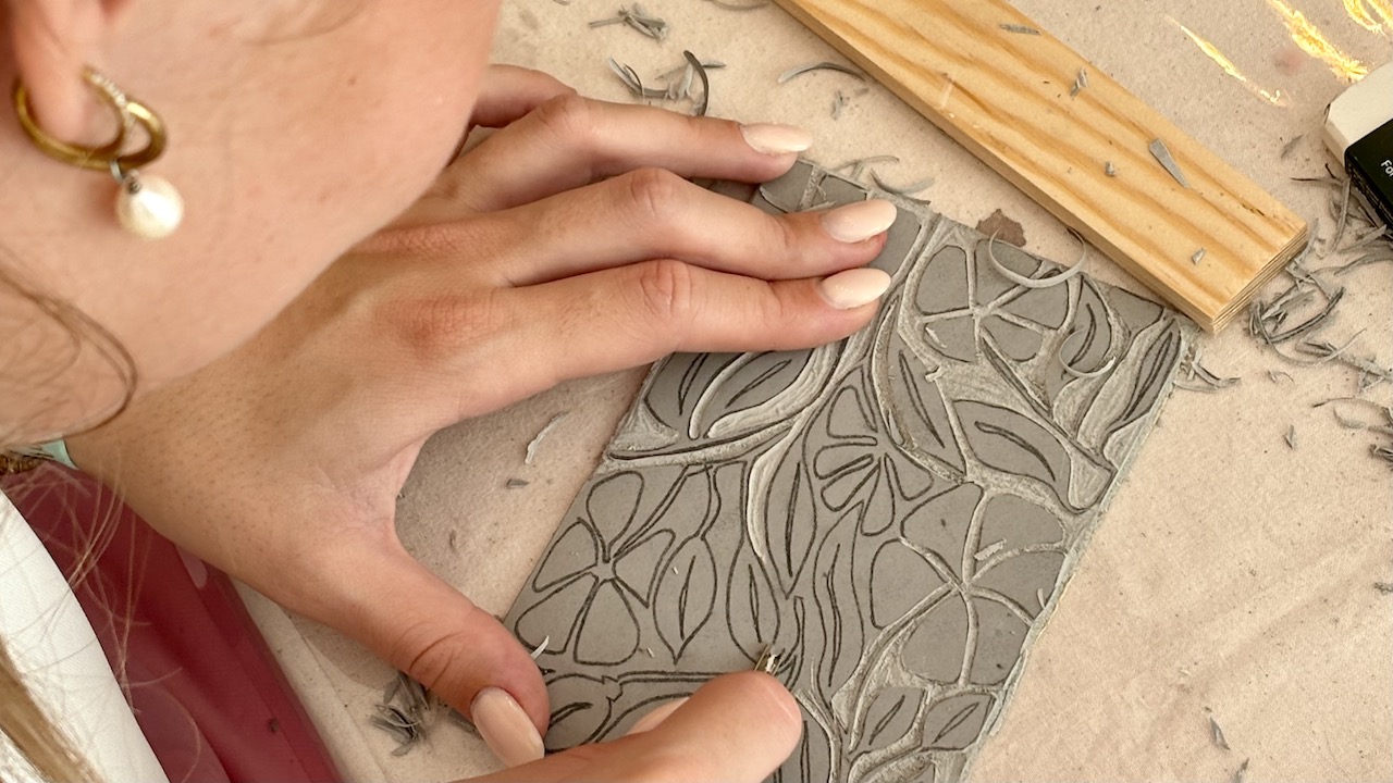 Person carving floral pattern into clay slab.