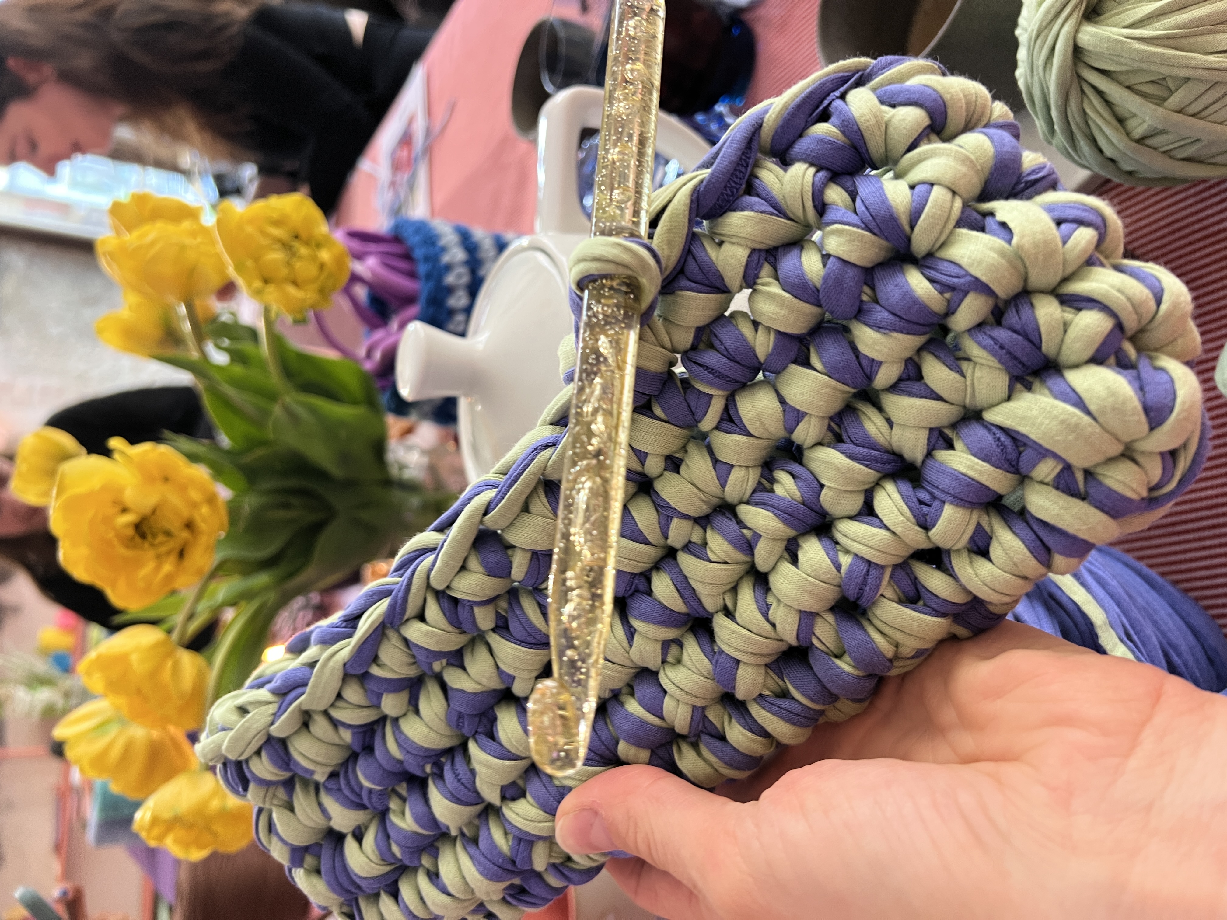 Hand holding crochet with yellow flowers in background.