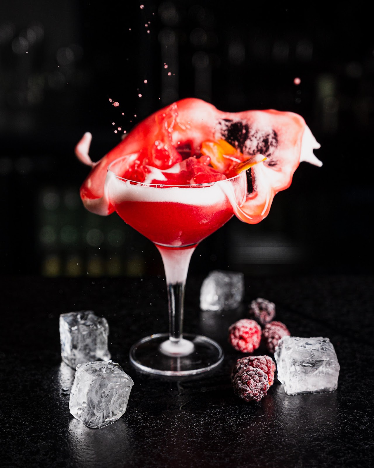 Red cocktail with splash, ice cubes, and berries.