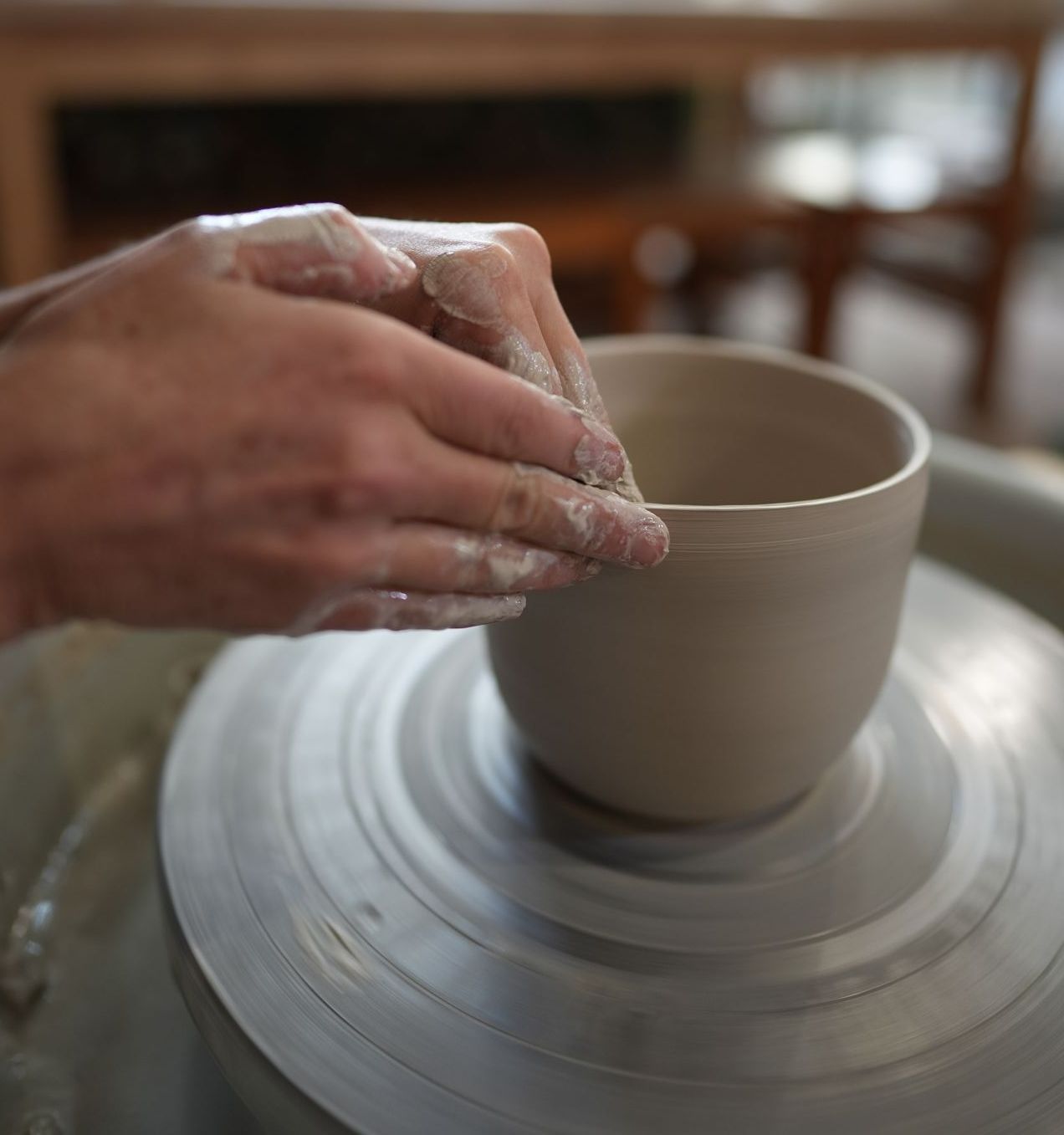 Hands shaping clay bowl on pottery wheel.