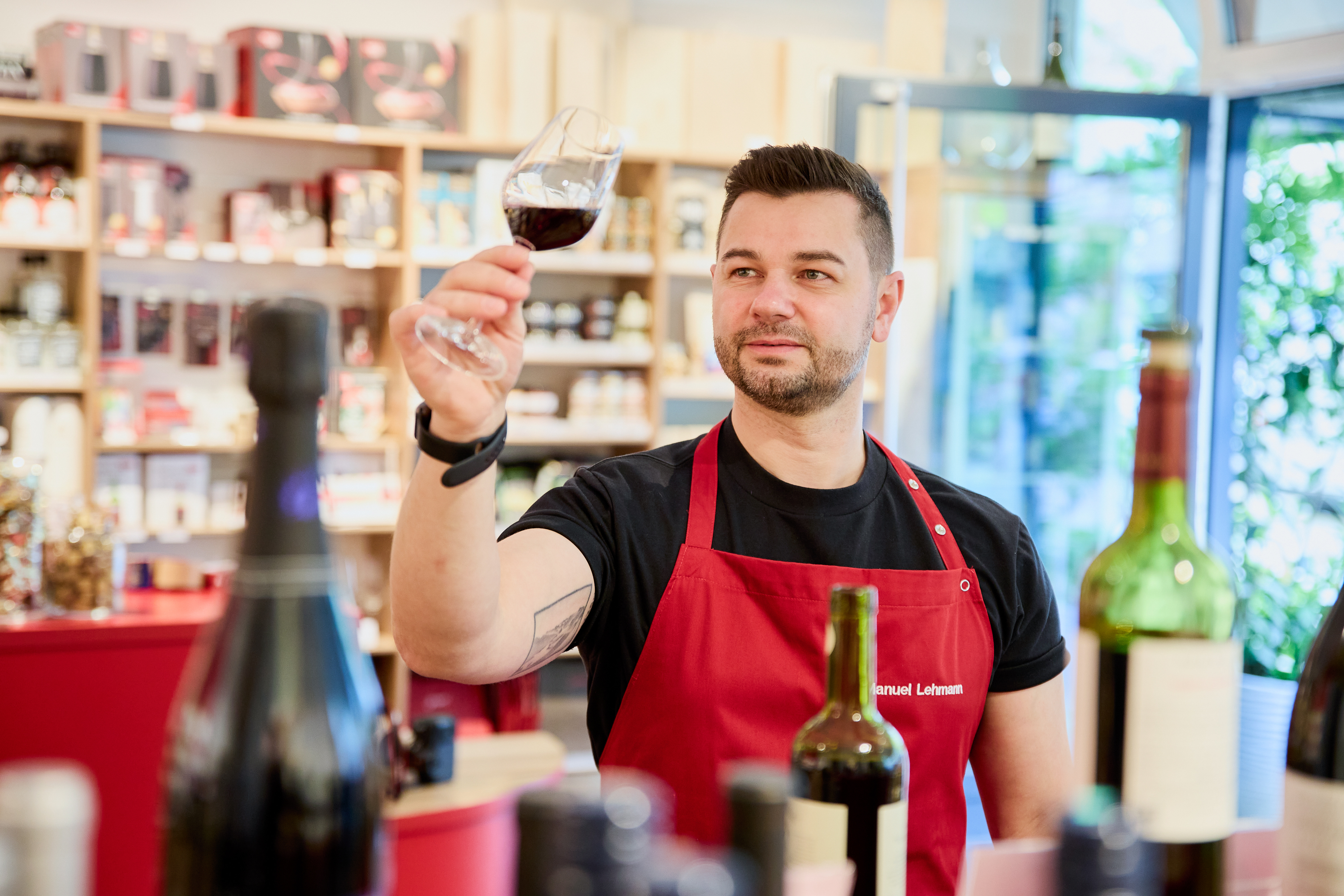 Mann in roter Schürze prüft Weinglas drinnen.