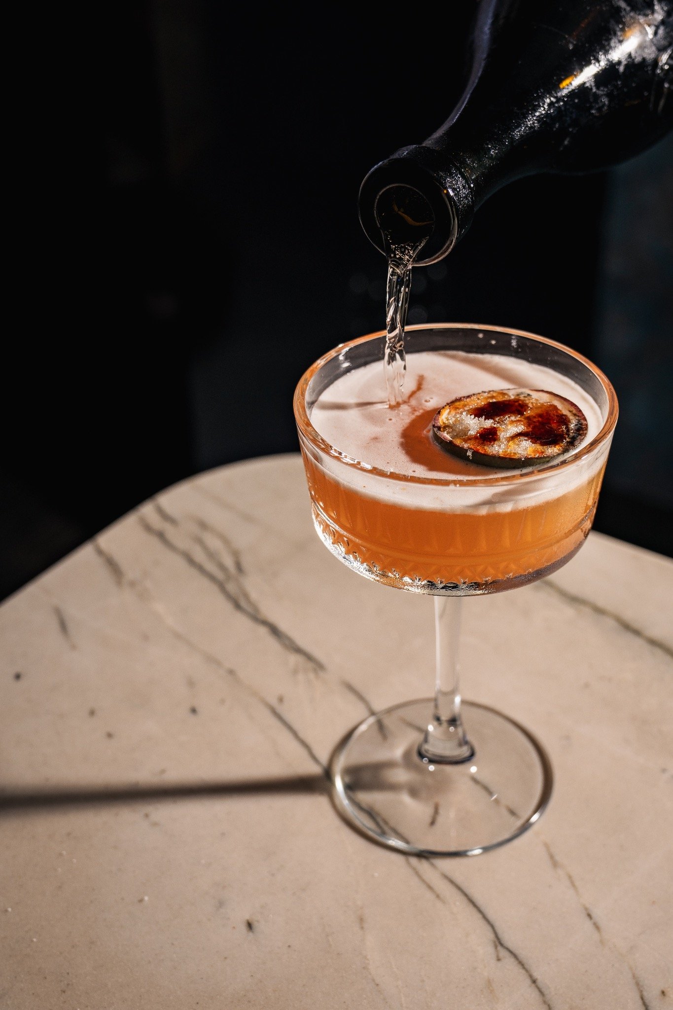 Cocktail being poured in a glass, marble table.