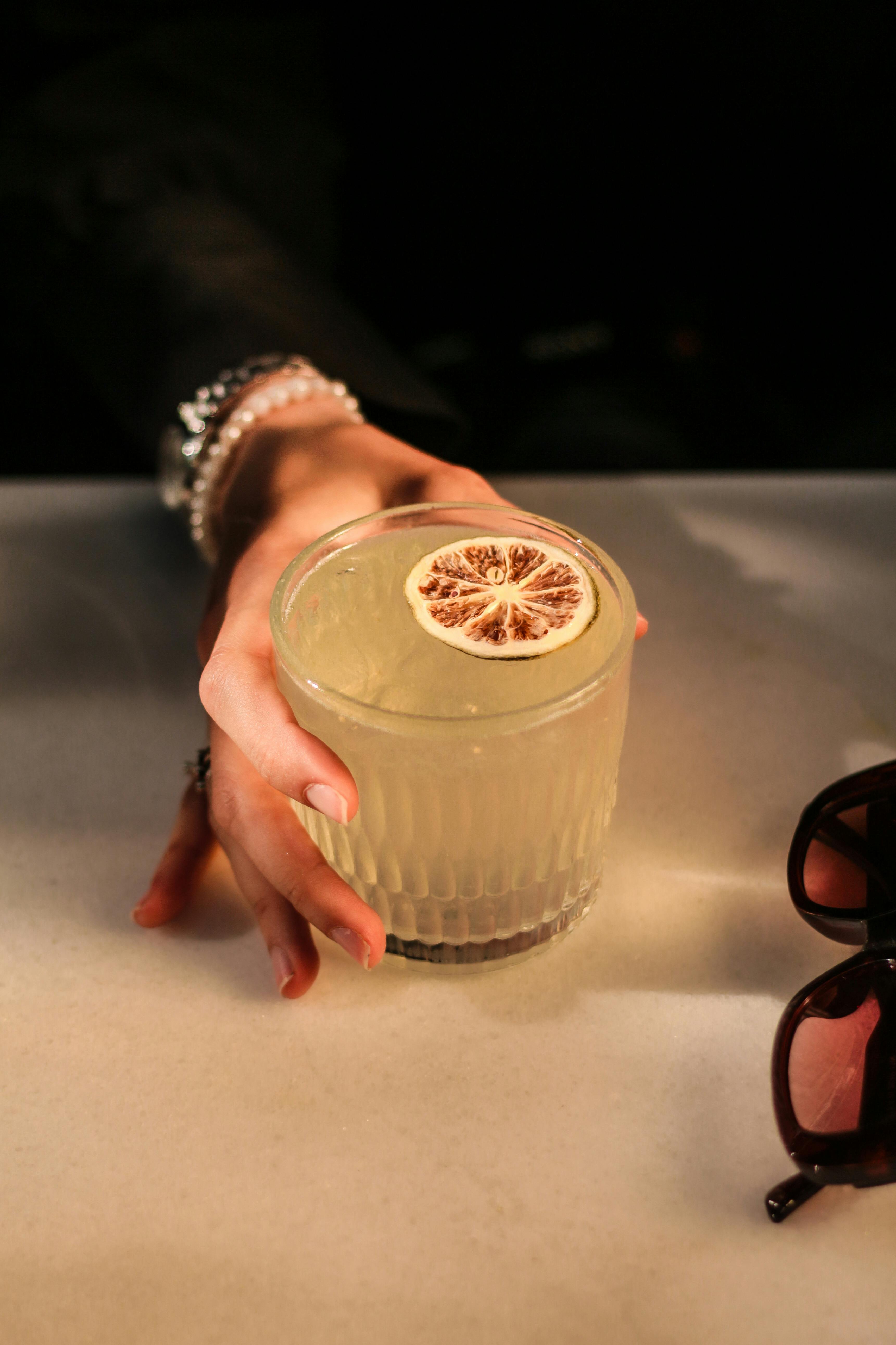 Hand holding cocktail with lemon garnish.