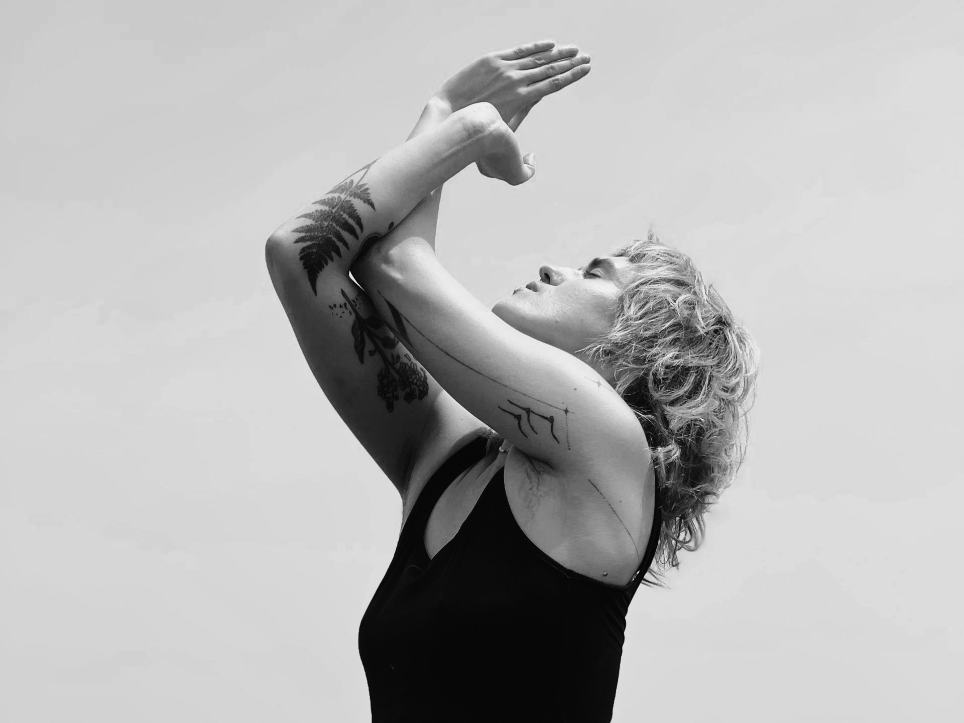 Person posing with arms crossed overhead outside.
