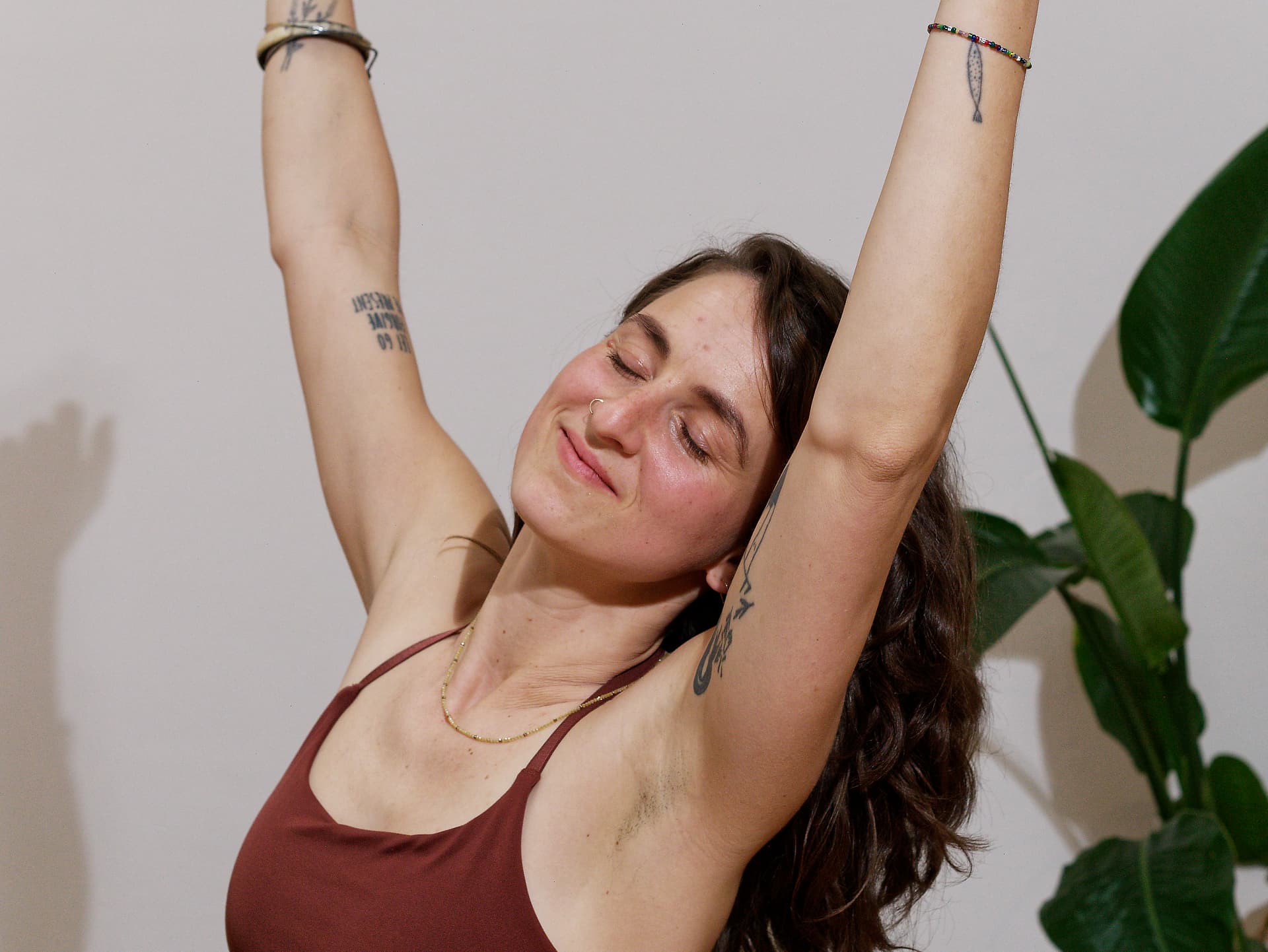 Woman stretching with arms raised, smiling indoors.