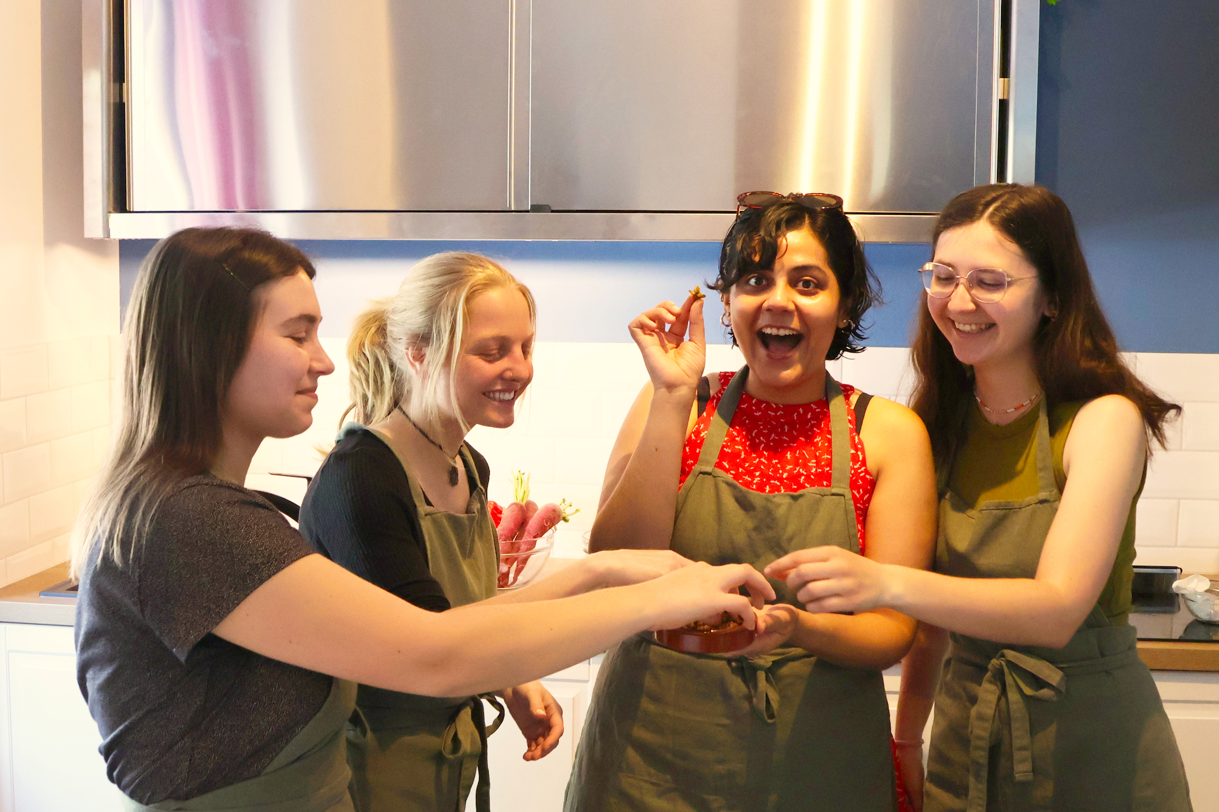 Four women cooking and laughing in a kitchen.