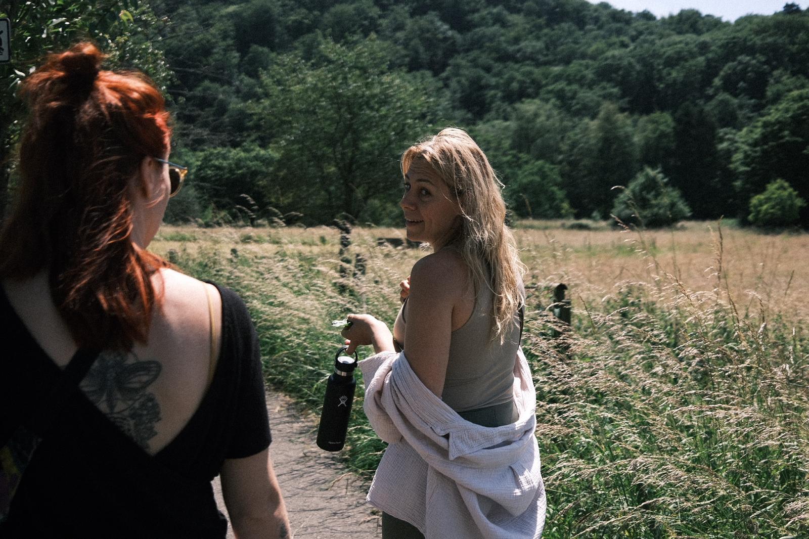 Two women walking through a grassy field.
