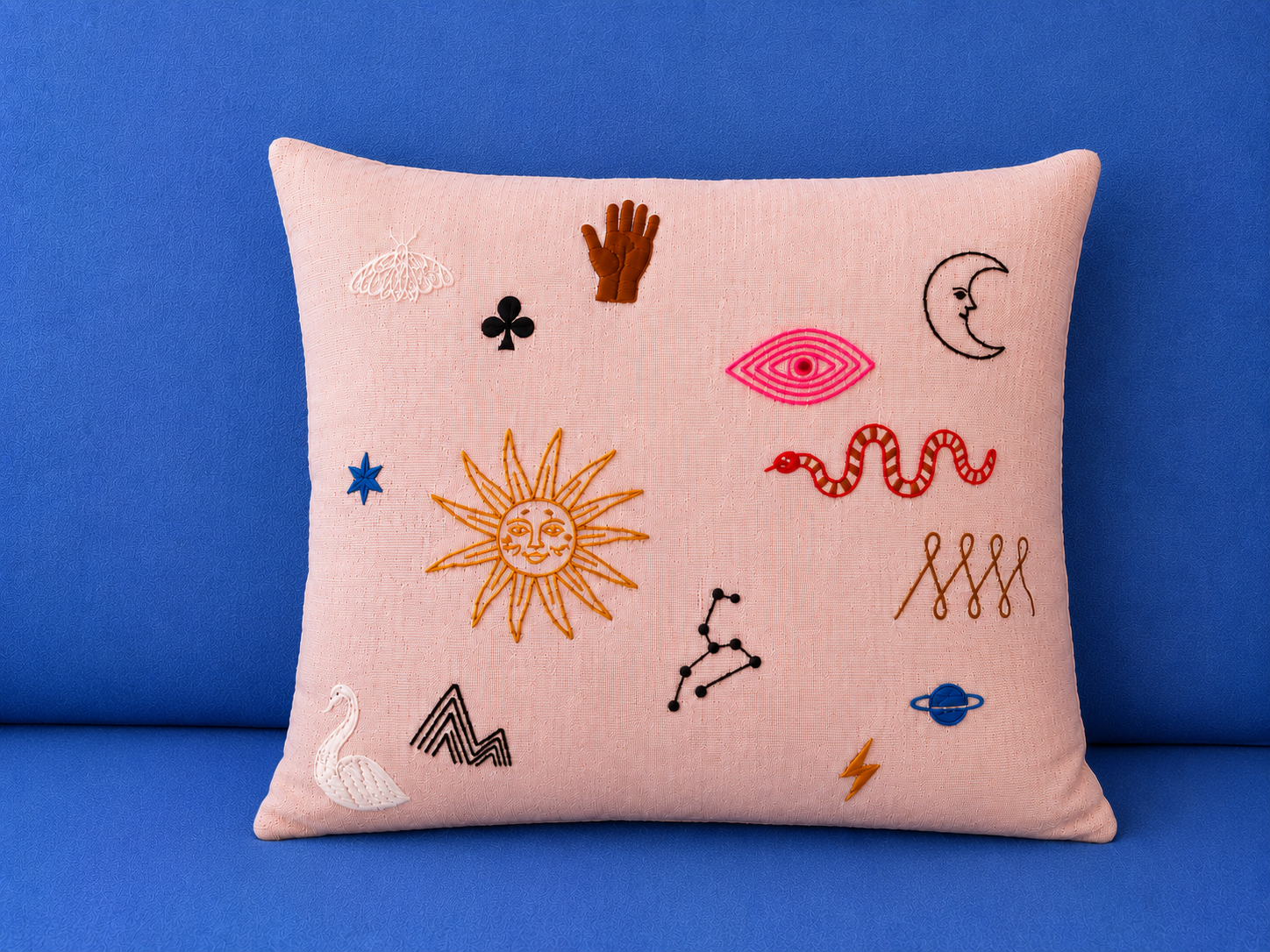 Embroidery symbols on pink cushion, blue background.