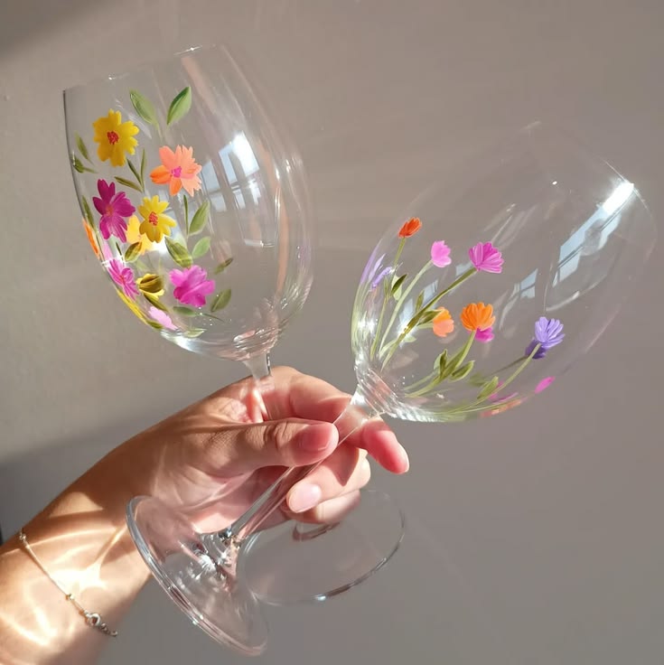 Hands holding floral-painted wine glasses.