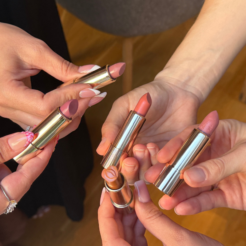 Five hands holding different lipstick shades.