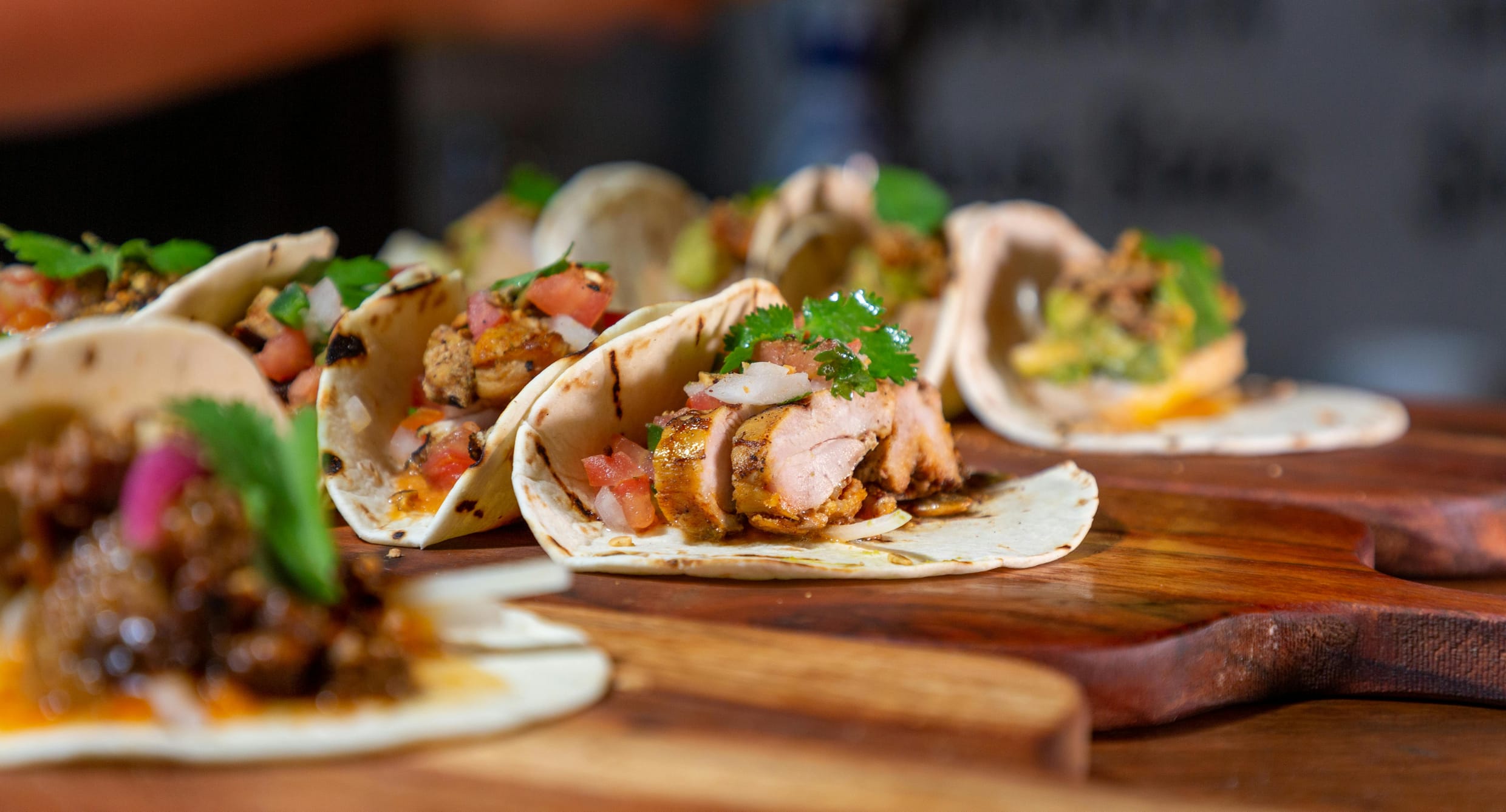 Tacos filled with chicken and vegetables on a board.