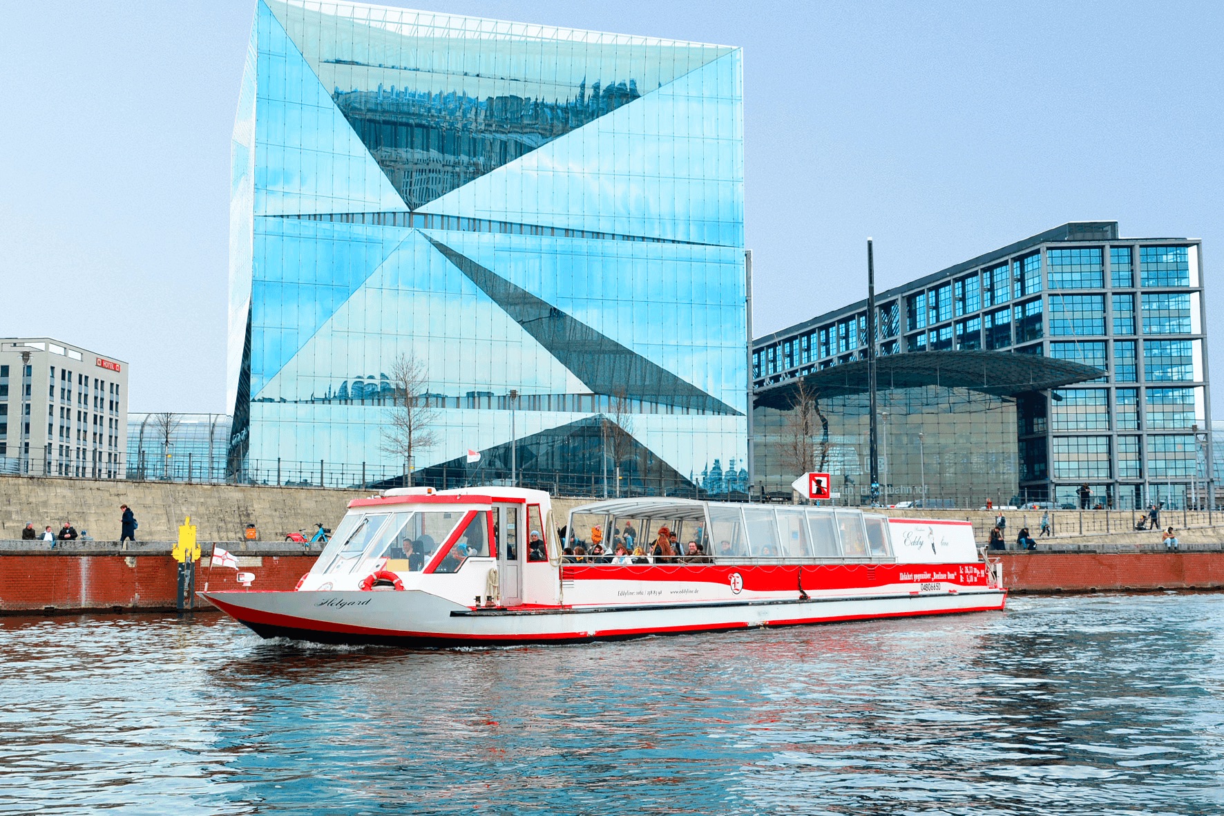Boot fährt auf Fluss neben modernen Gebäuden.