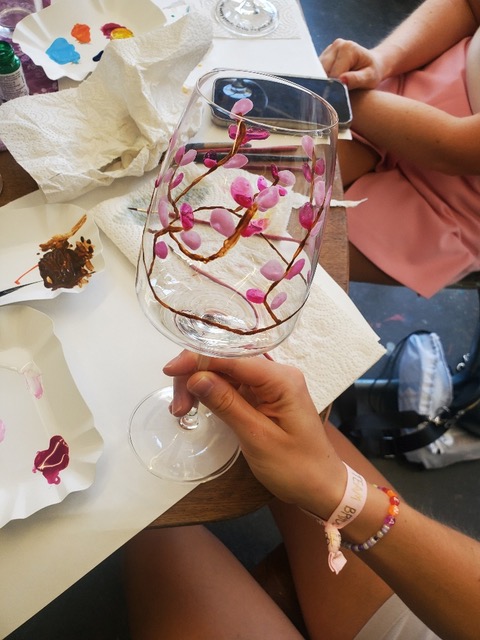 Weinglas mit rosa Blumen bemalt, Hand haltend.