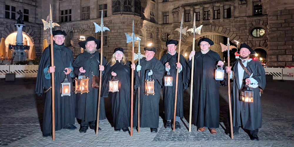 Gruppe hält Laternen vor historischem Gebäude.