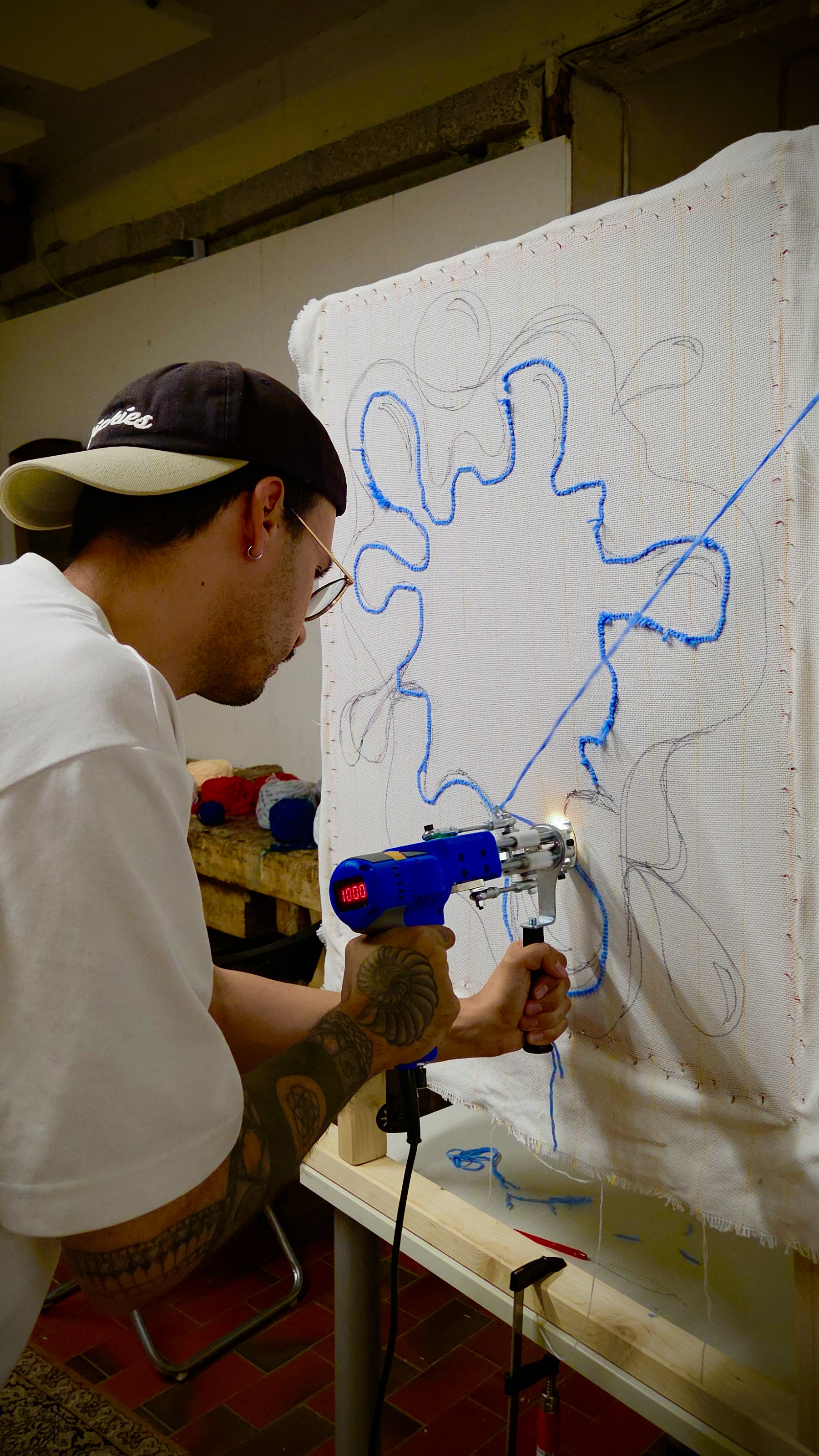 Person using tufting gun on canvas indoors.
