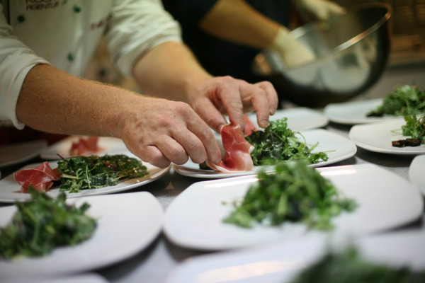 Koch platziert Schinken auf Salat auf Tellern in Küche.