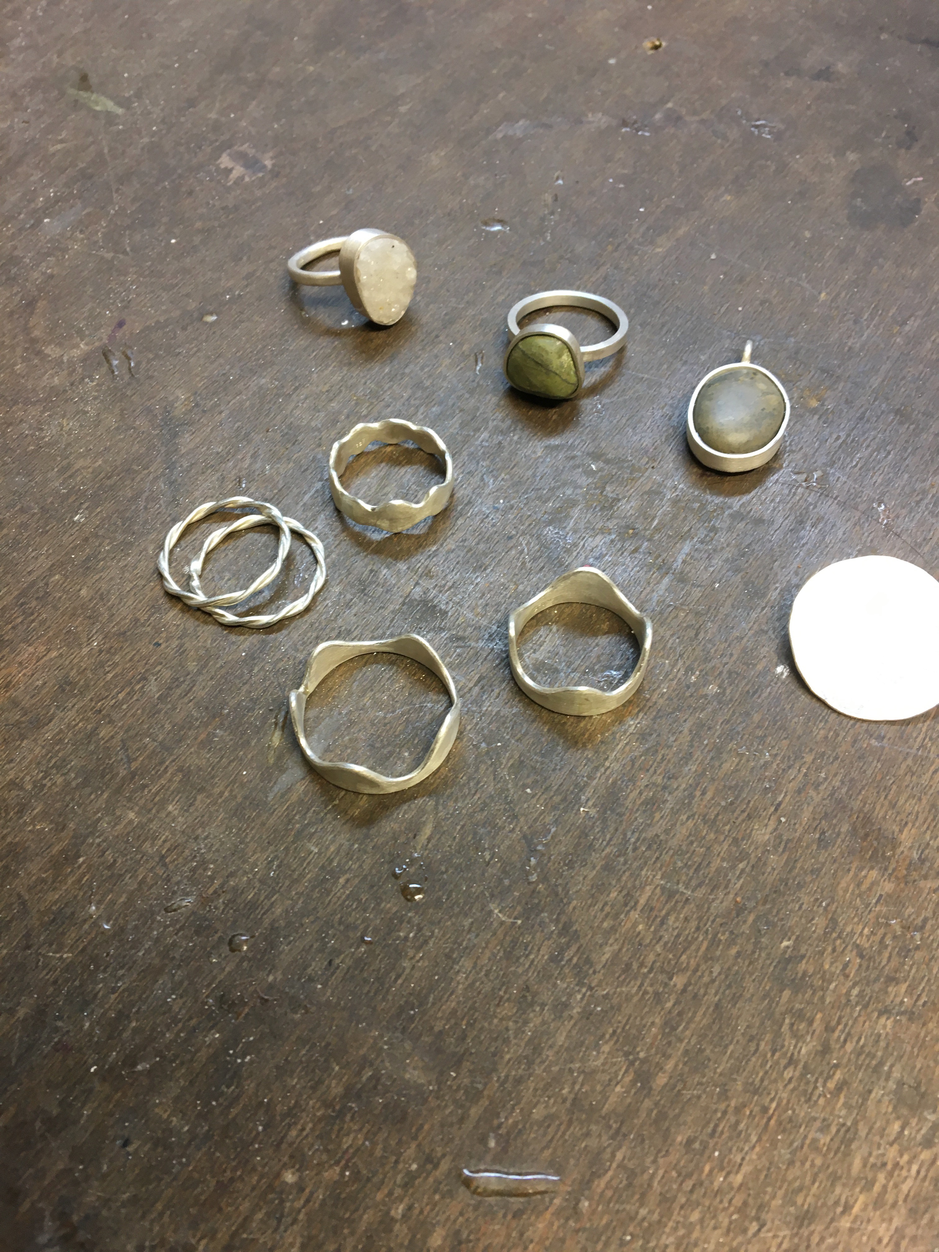 Silver rings and pendant on wooden surface.