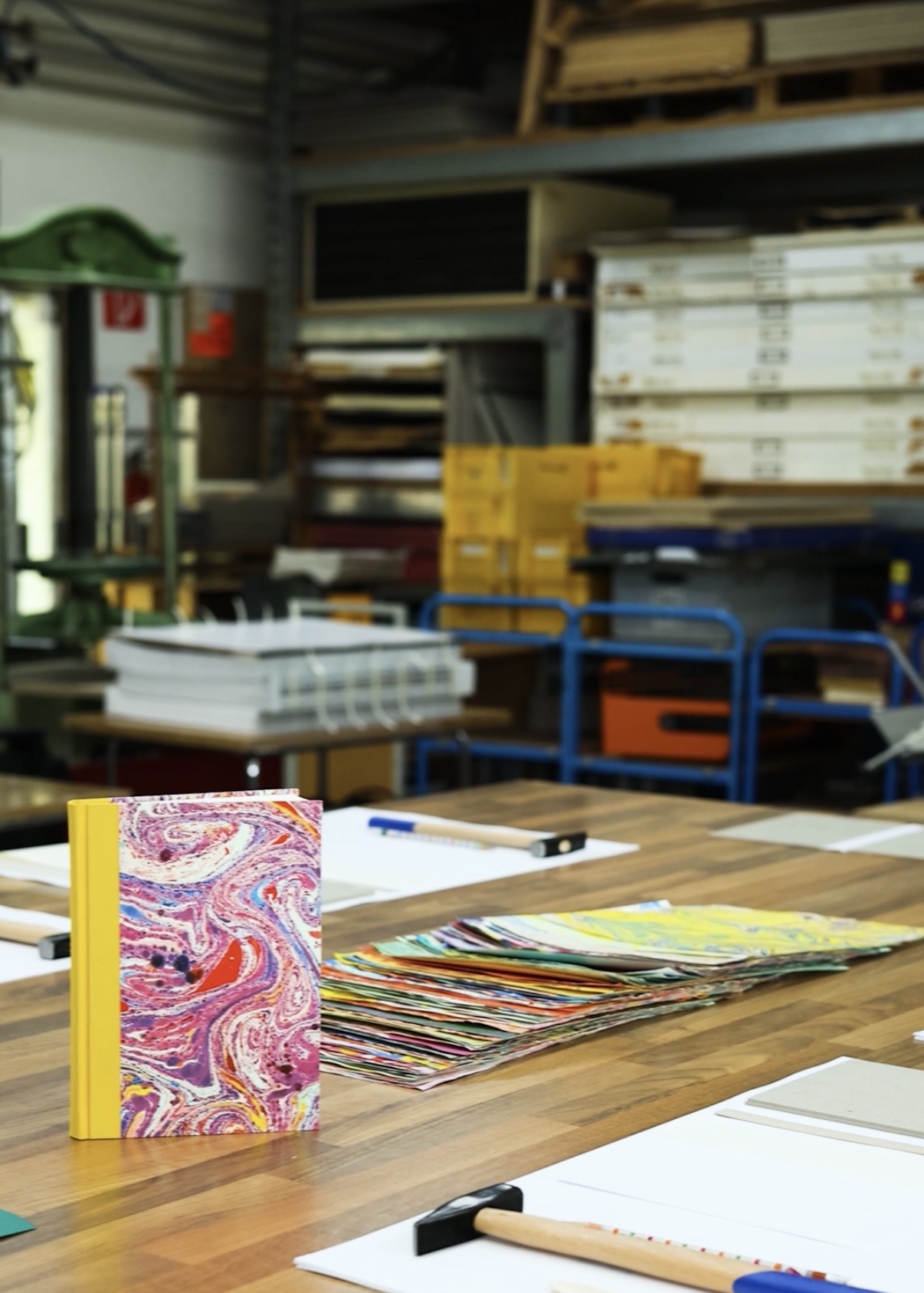 Buntes Buch auf Werkstatt-Tisch, umgeben von Papieren.