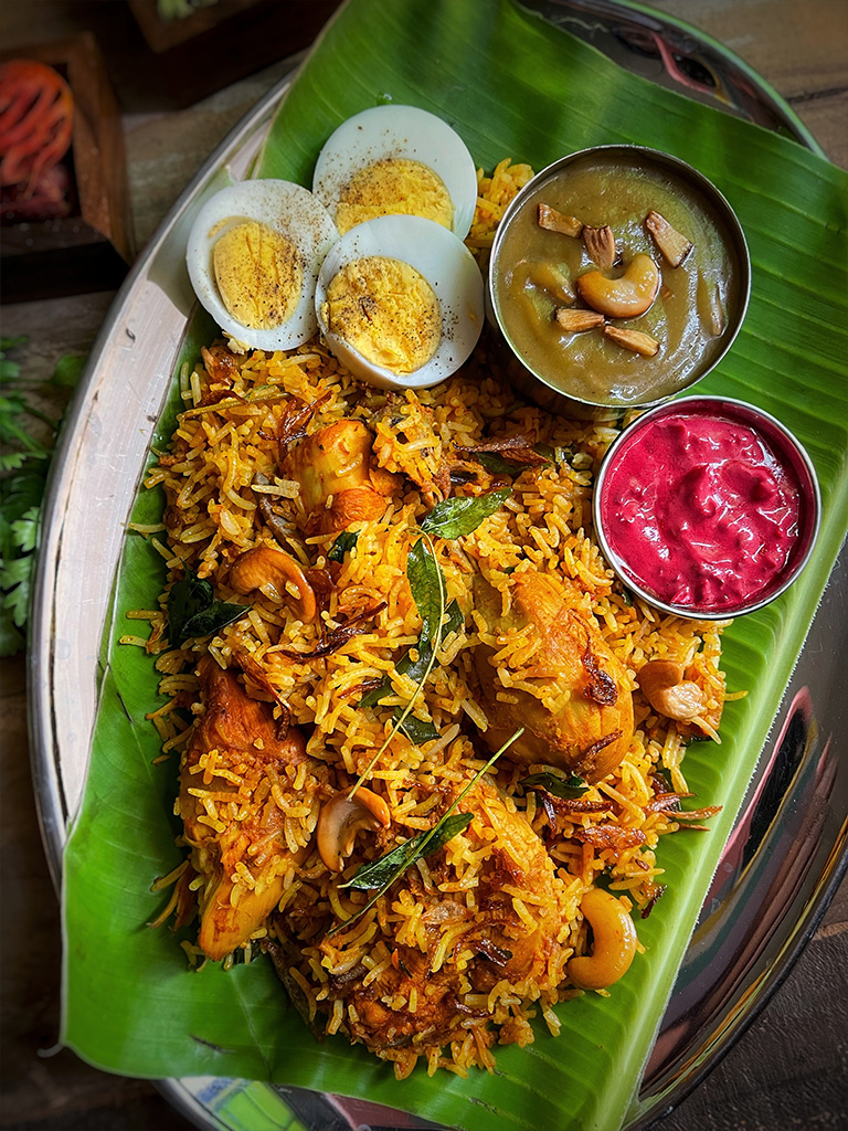 Biryani served on banana leaf with sauces.