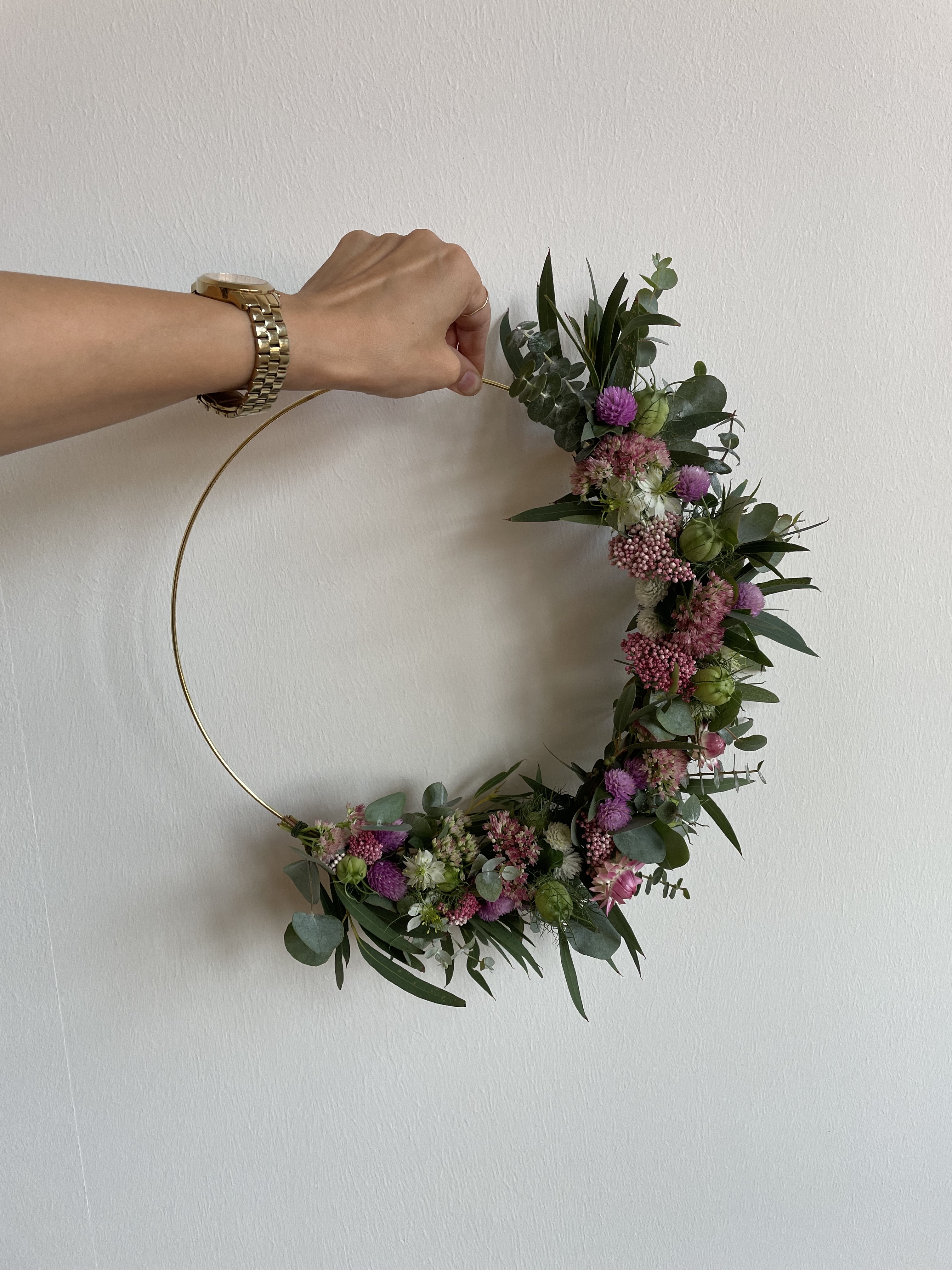 Hand hält einen Blumenkranz, dekorativ an der Wand.