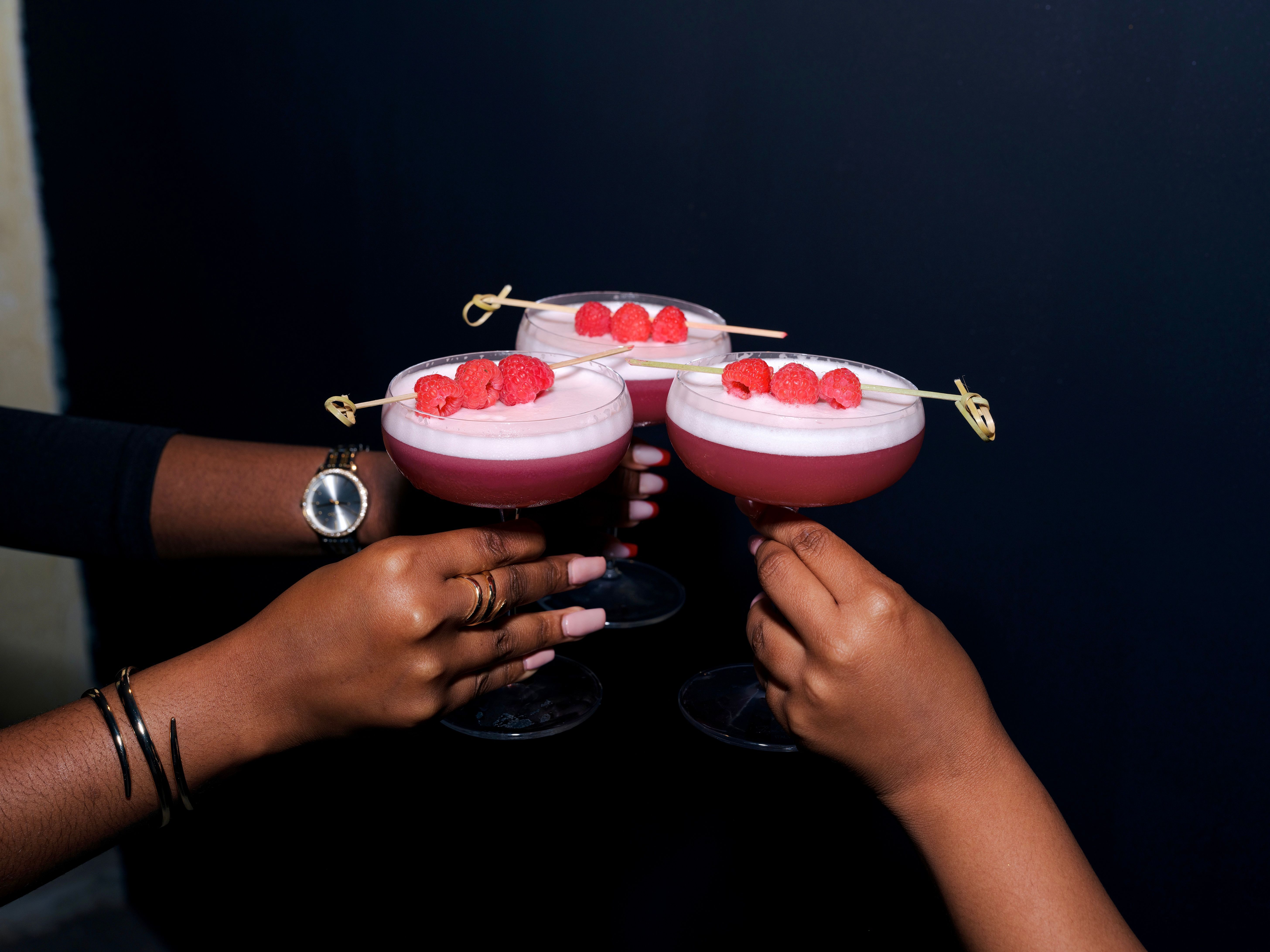 Three glasses raised with berry cocktails.