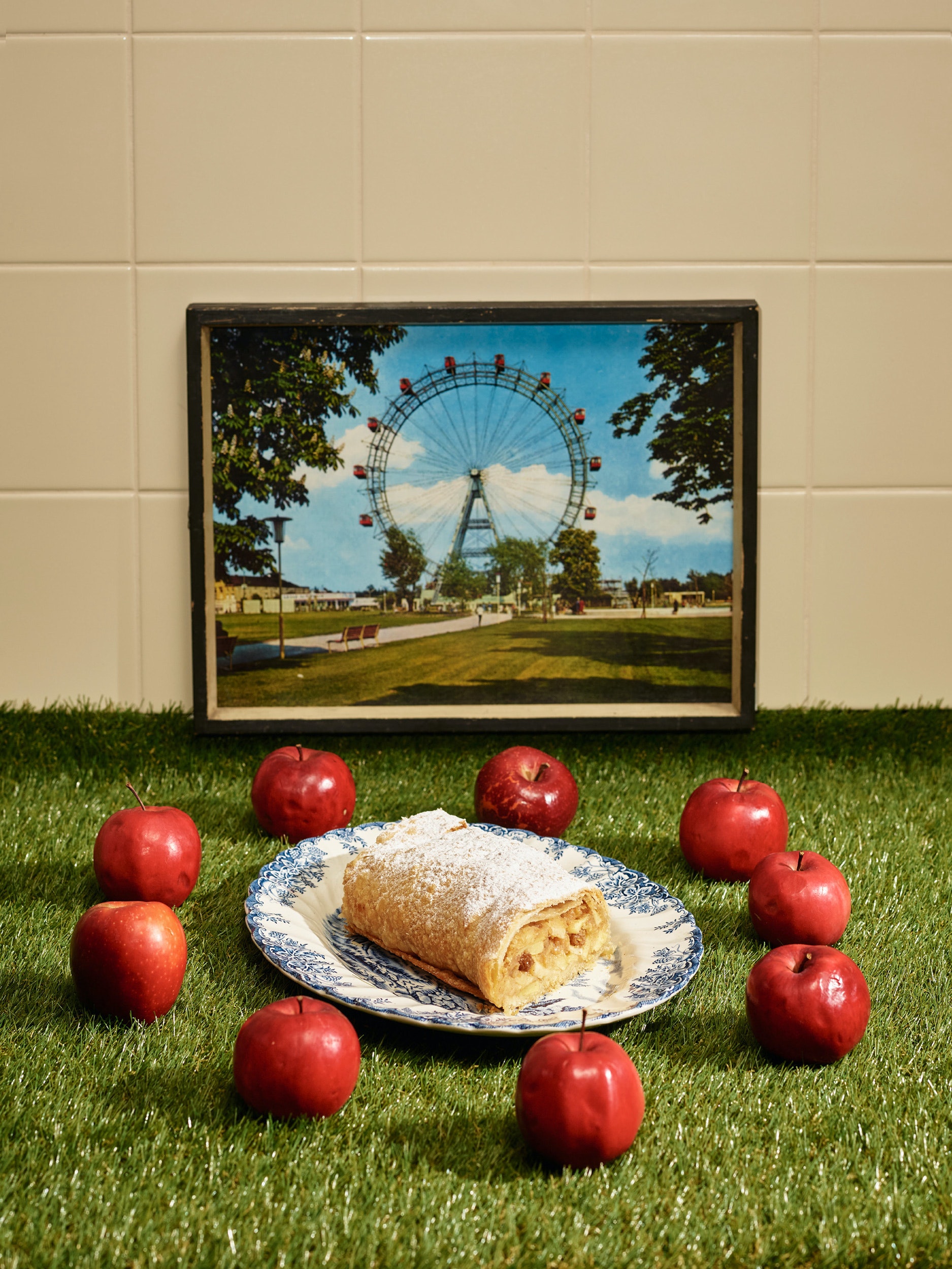 Apfelstrudel liegt auf Teller, umgeben von roten Äpfeln.
