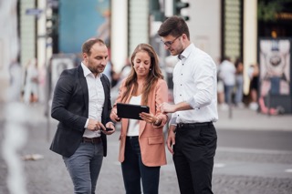 Three people are looking at a tablet on the street.