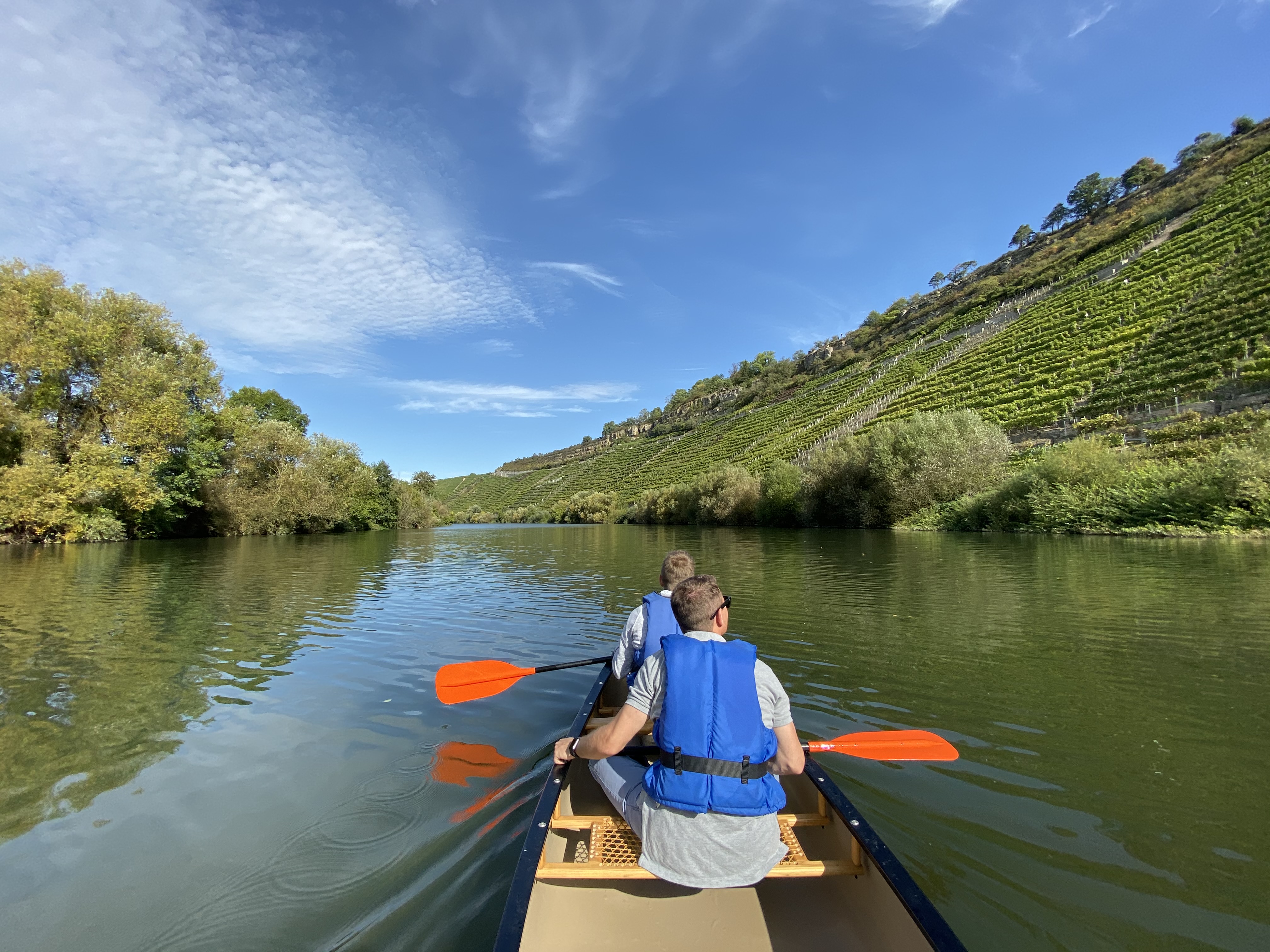 Zwei Personen rudern in einem Boot auf einem ruhigen Fluss.