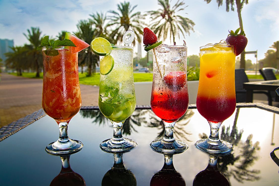 Bunte Cocktails stehen auf einem Tisch, umgeben von Palmen.