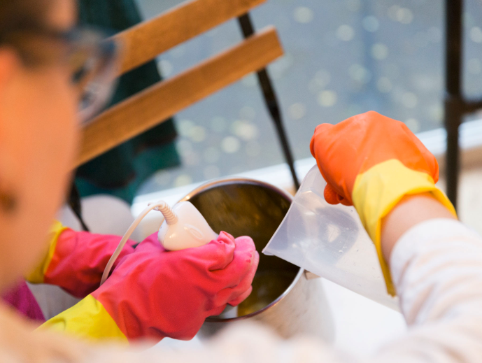 A person with gloves mixes liquid in a pot.