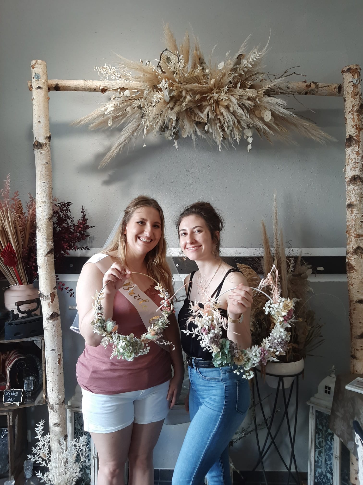Two women hold blooming wreaths in a decorated room.