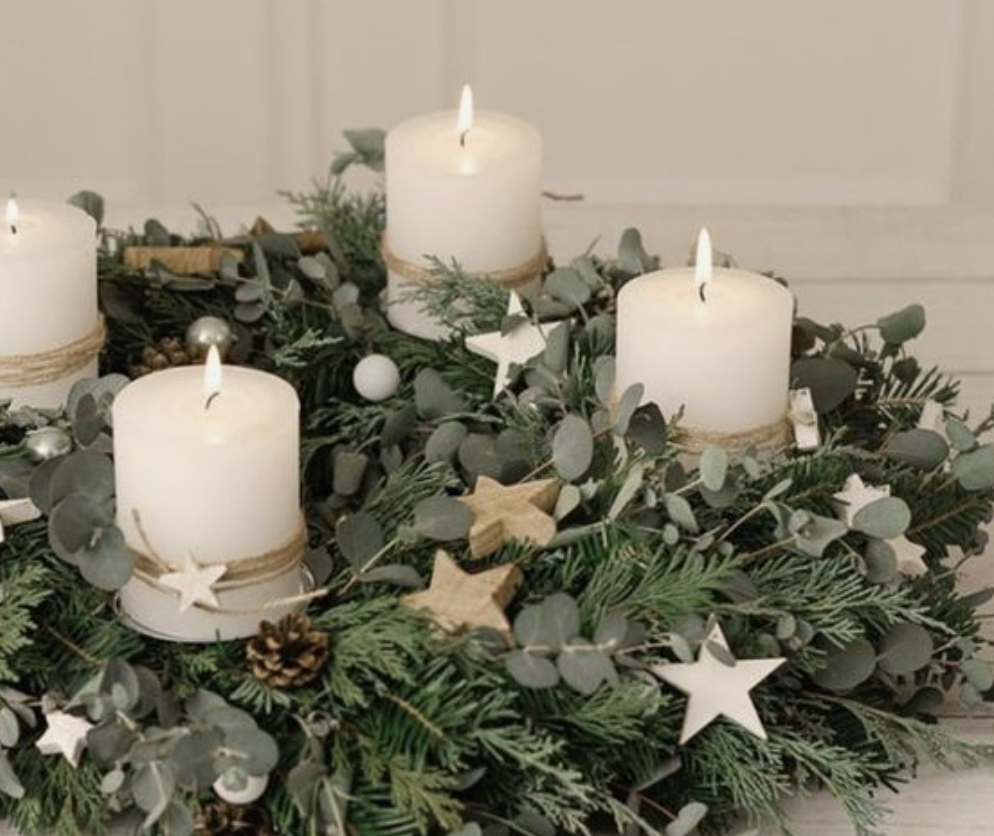 Weiße Kerzen stehen auf einem Adventskranz aus Tannenzweigen.