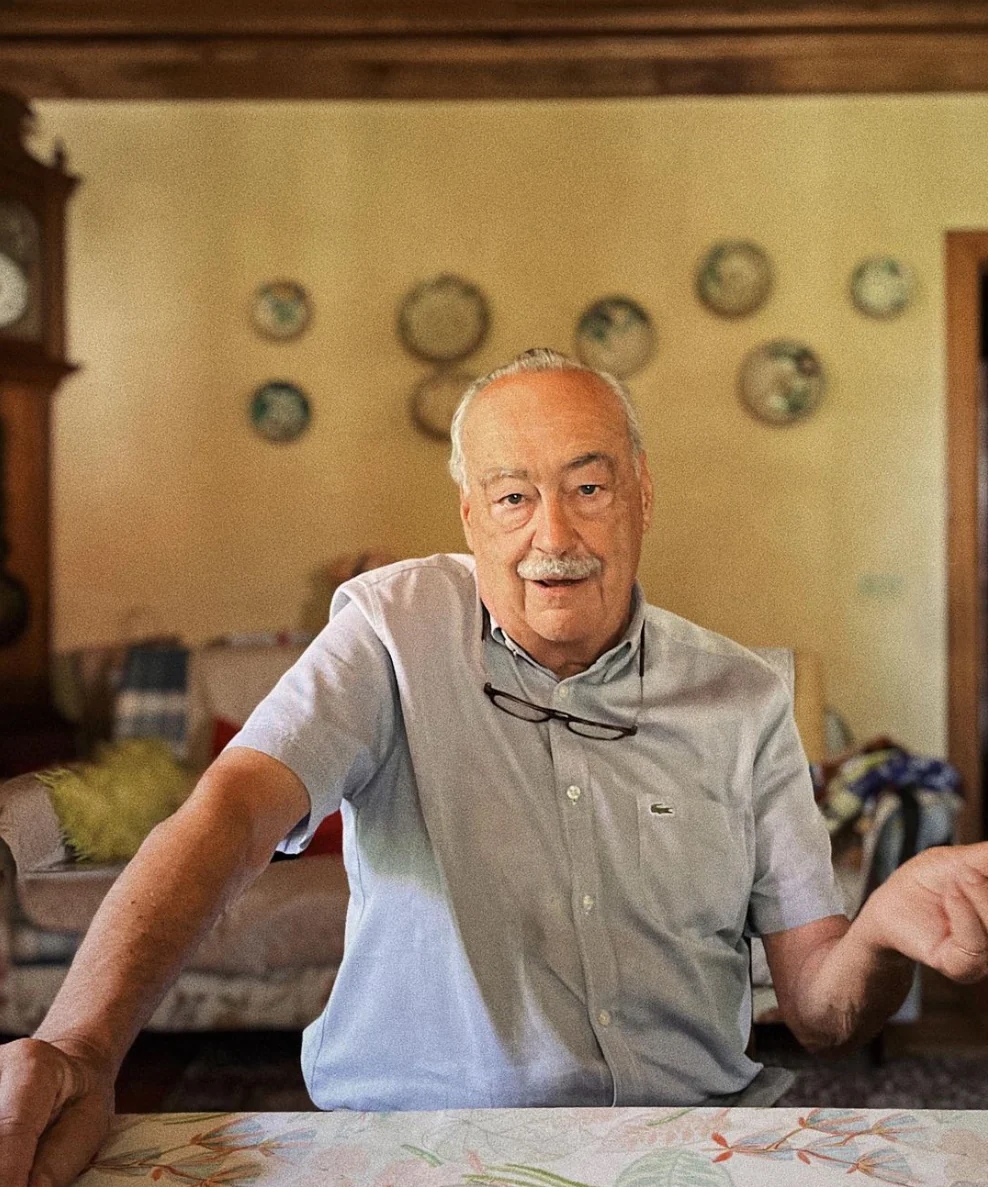 Elderly man sits at the table and talks in the living room.