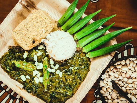 Grünes Gericht mit Reis, Okra und Brot auf Holzplatte.