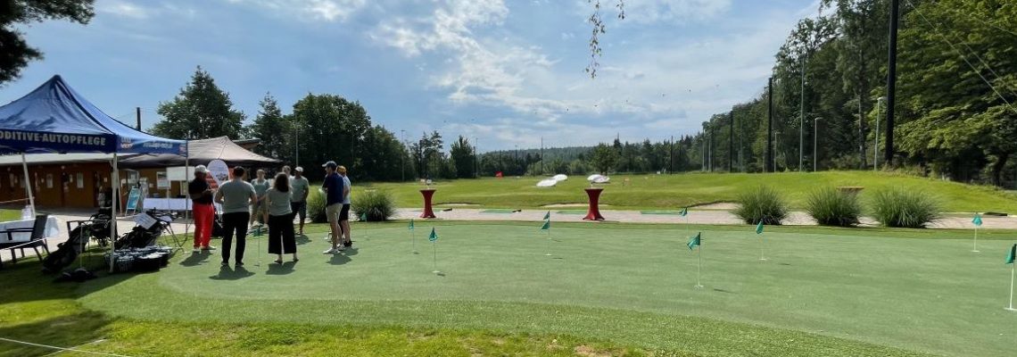 Group of people standing on golf course, under blue sky.