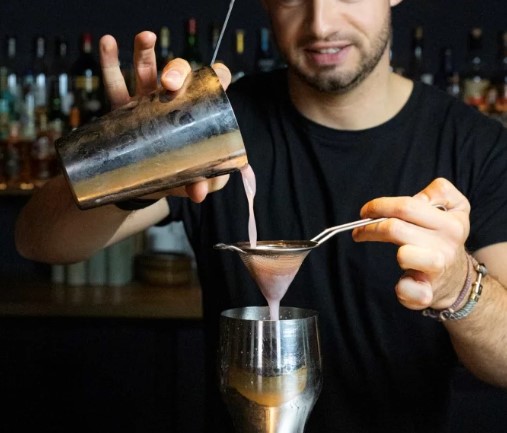 Barkeeper gießt einen Cocktail durch einen Sieb in ein Glas.