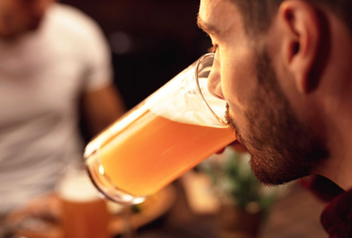 A man drinks from a glass of beer in a bar.