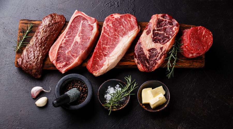 Pieces of meat lie on a wooden board with spices.