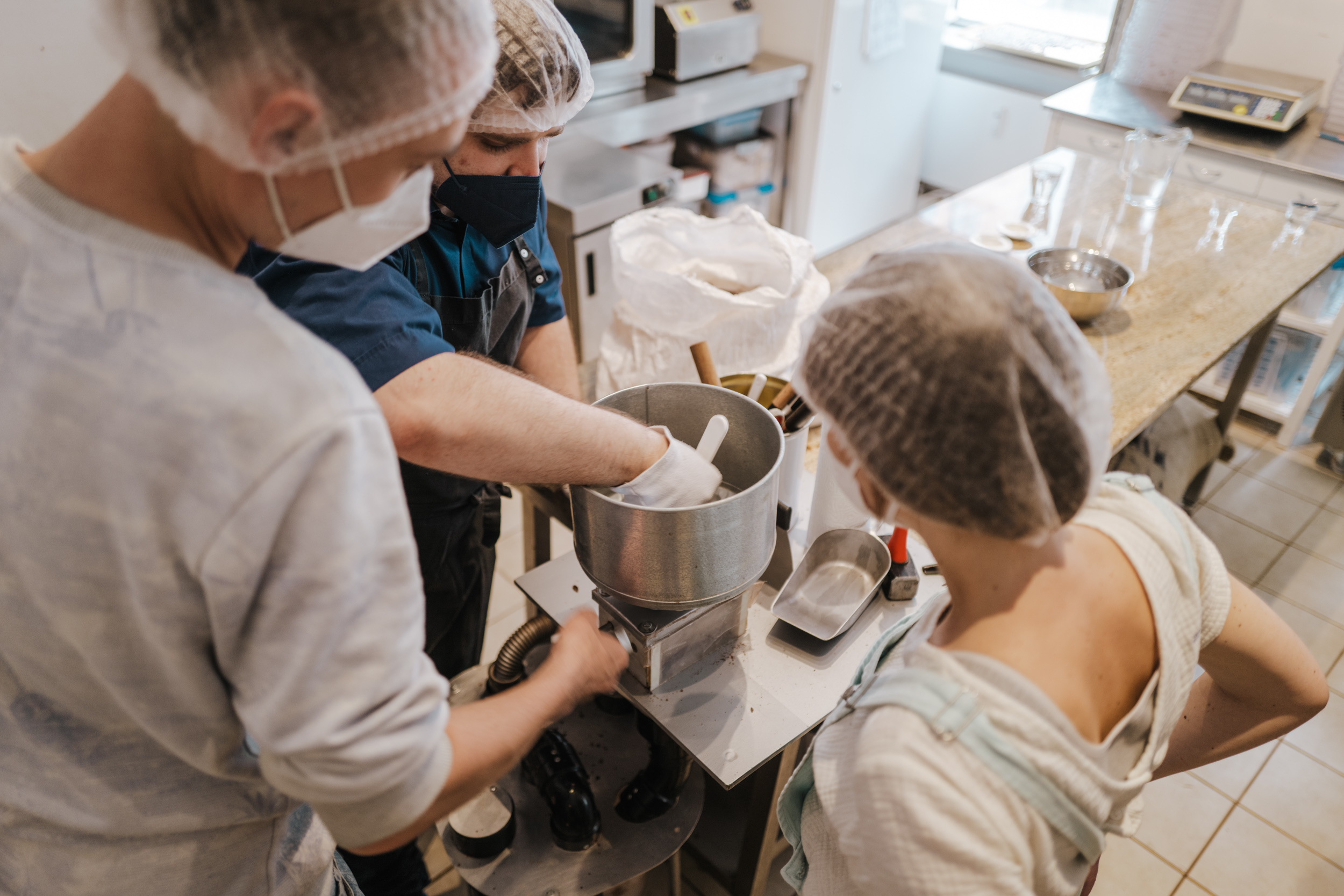 Three people work together on a machine in the kitchen.