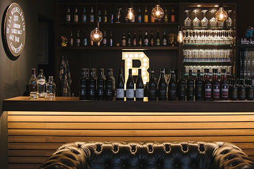 Bar mit Getränken und beleuchtetem Buchstaben „R“ im Hintergrund.