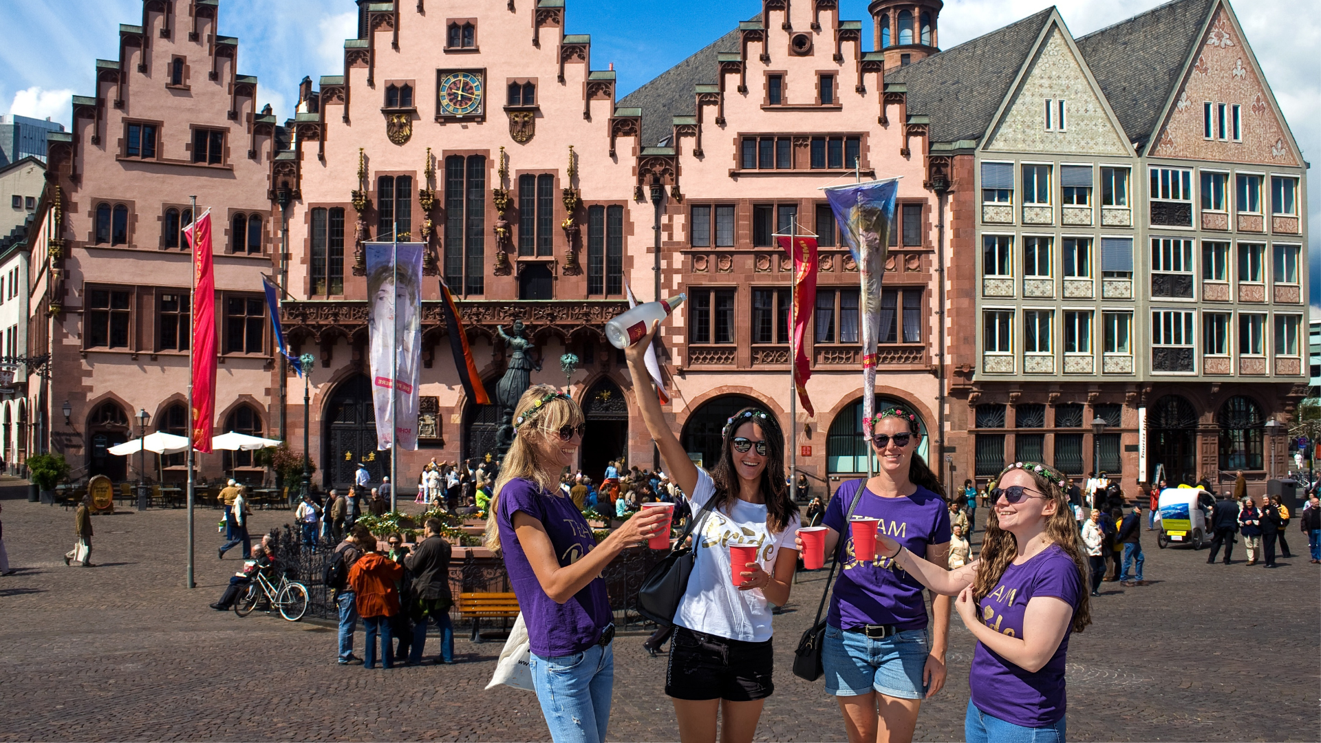Vier Frauen feiern mit Getränken auf einem Platz.