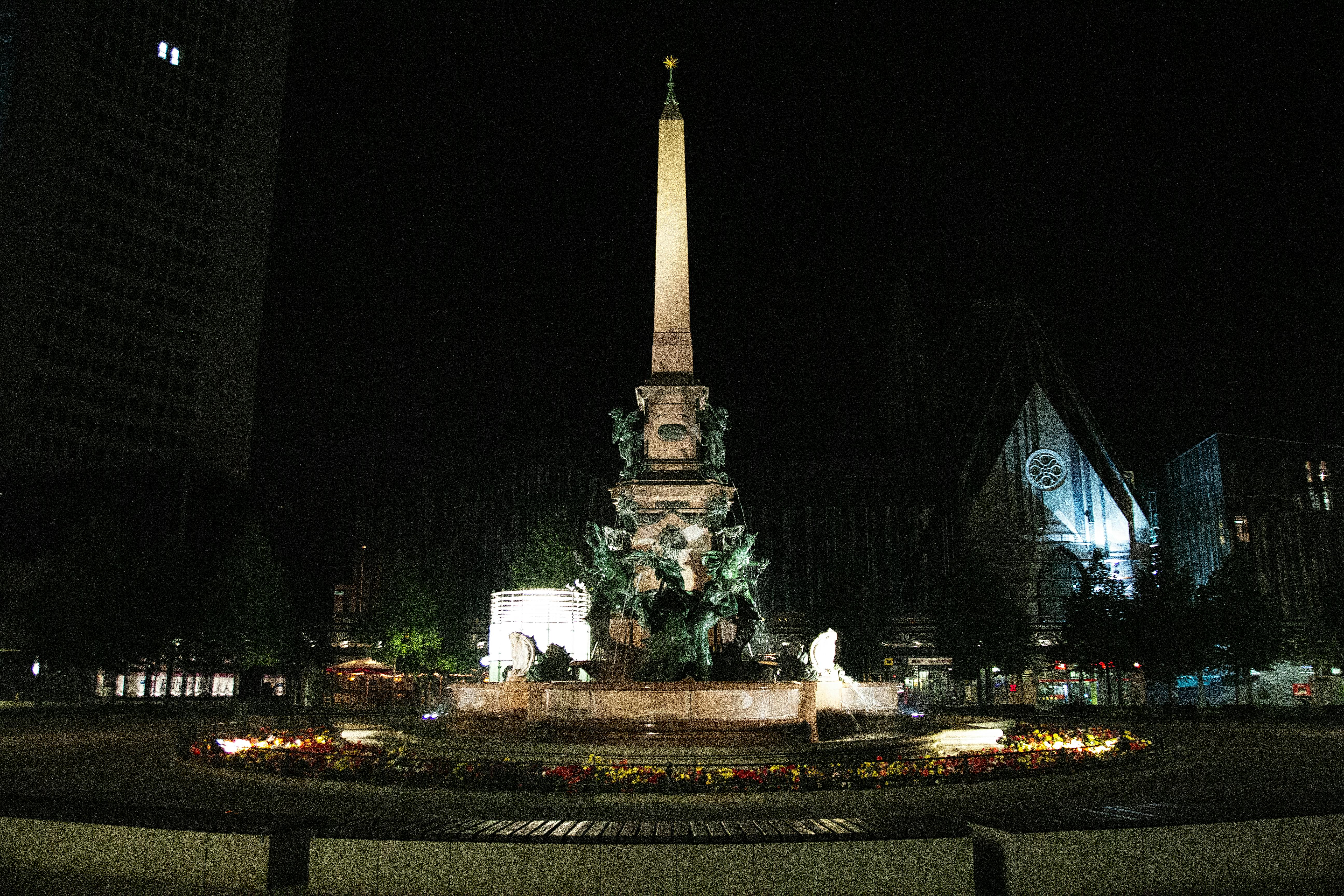 An obelisk stands at night surrounded by a fountain.