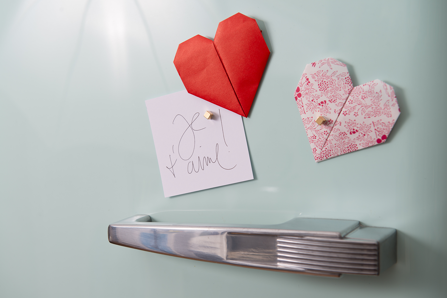 Roter und rosa Origami-Herzen hängen an Kühlschranktür.
