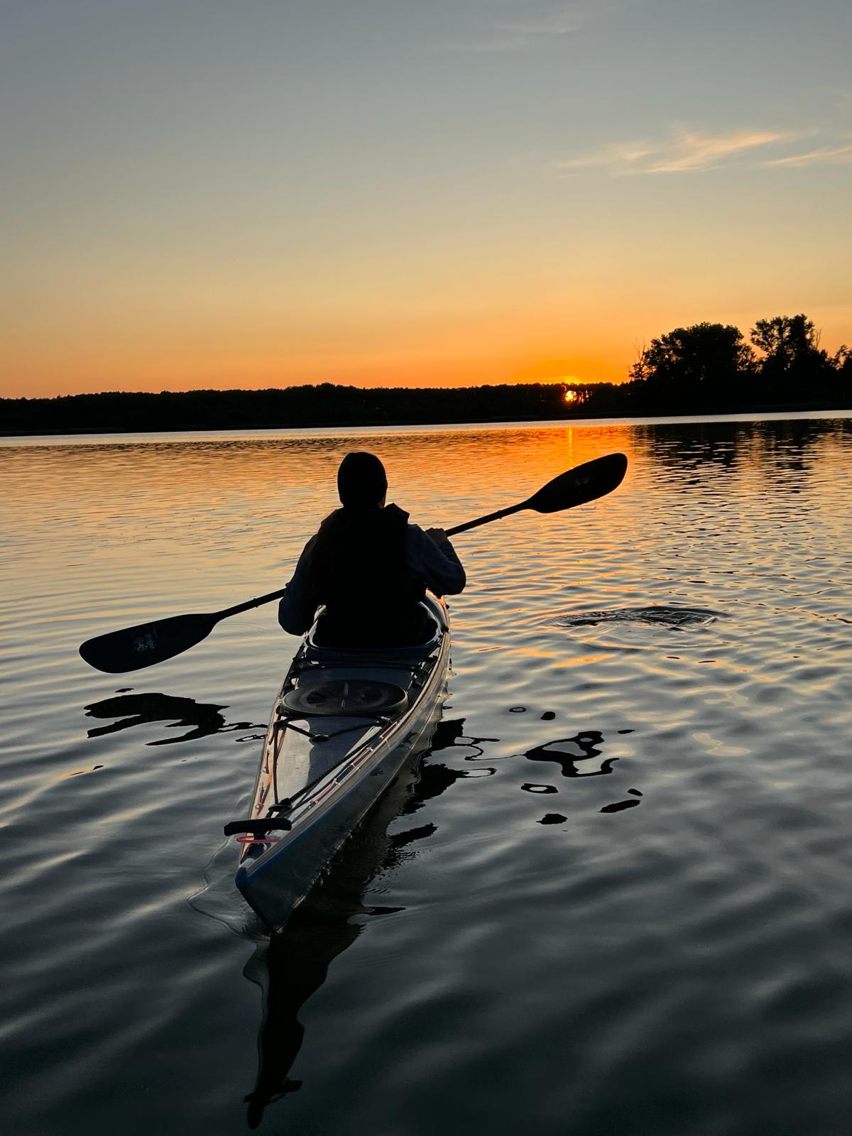 Kajakfahrer paddelt im Sonnenuntergang auf ruhigem Wasser.
