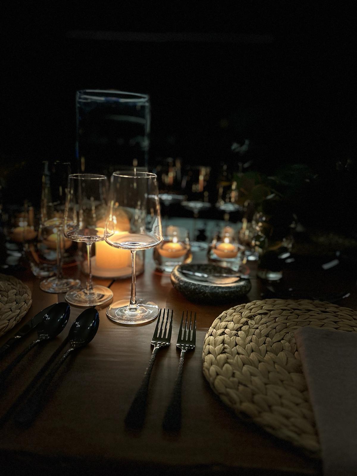 Zwei Gläser stehen auf einem gedeckten Tisch bei Kerzenlicht.